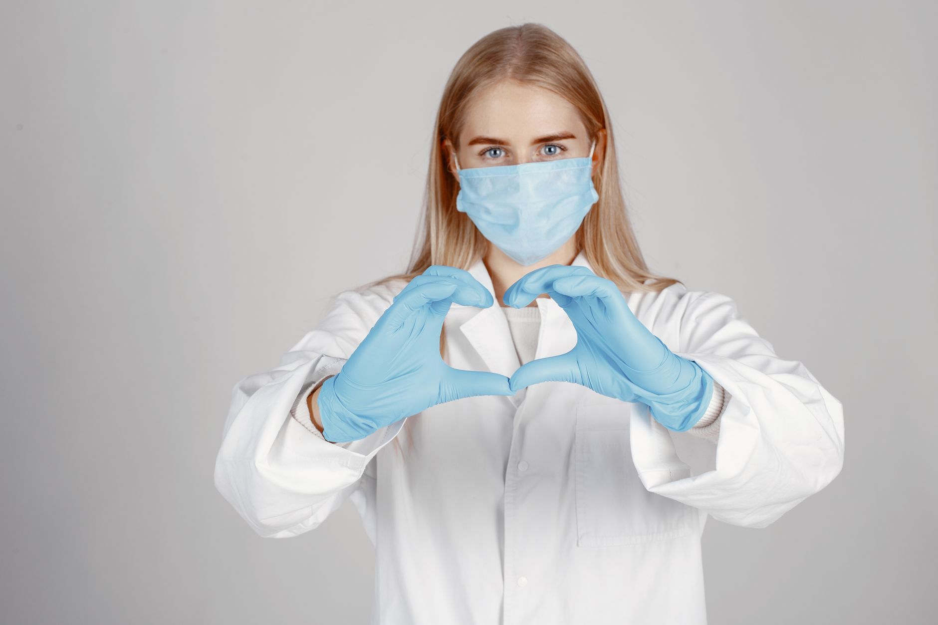 Healthcare worker wearing mask and gloves showing a heart shape with hands symbolizing care.