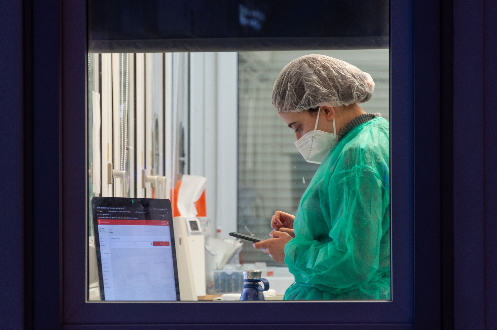 A healthcare worker in protective clothing uses a phone in a laboratory, emphasizing modern medical practices.