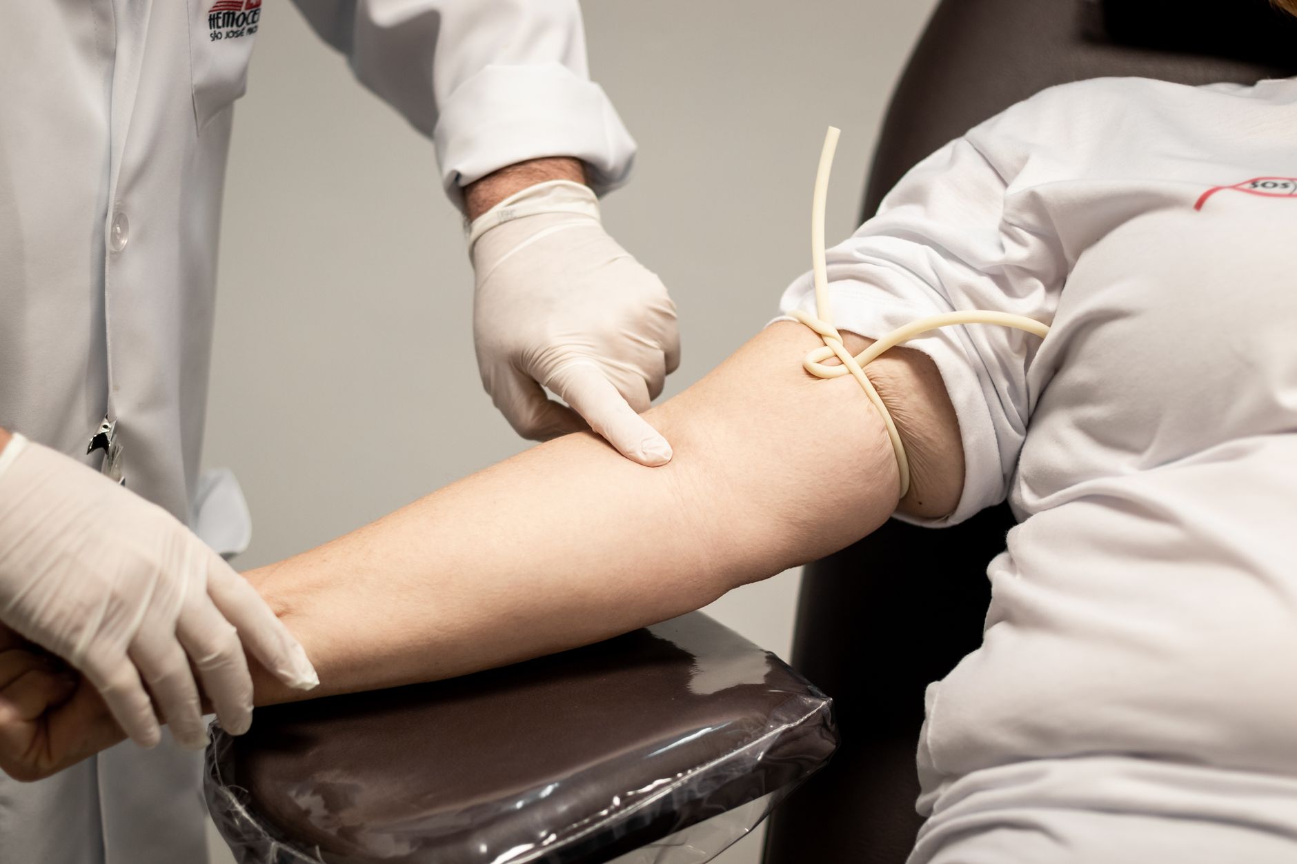 Medical professional wearing gloves preparing patient for blood draw using a tourniquet.