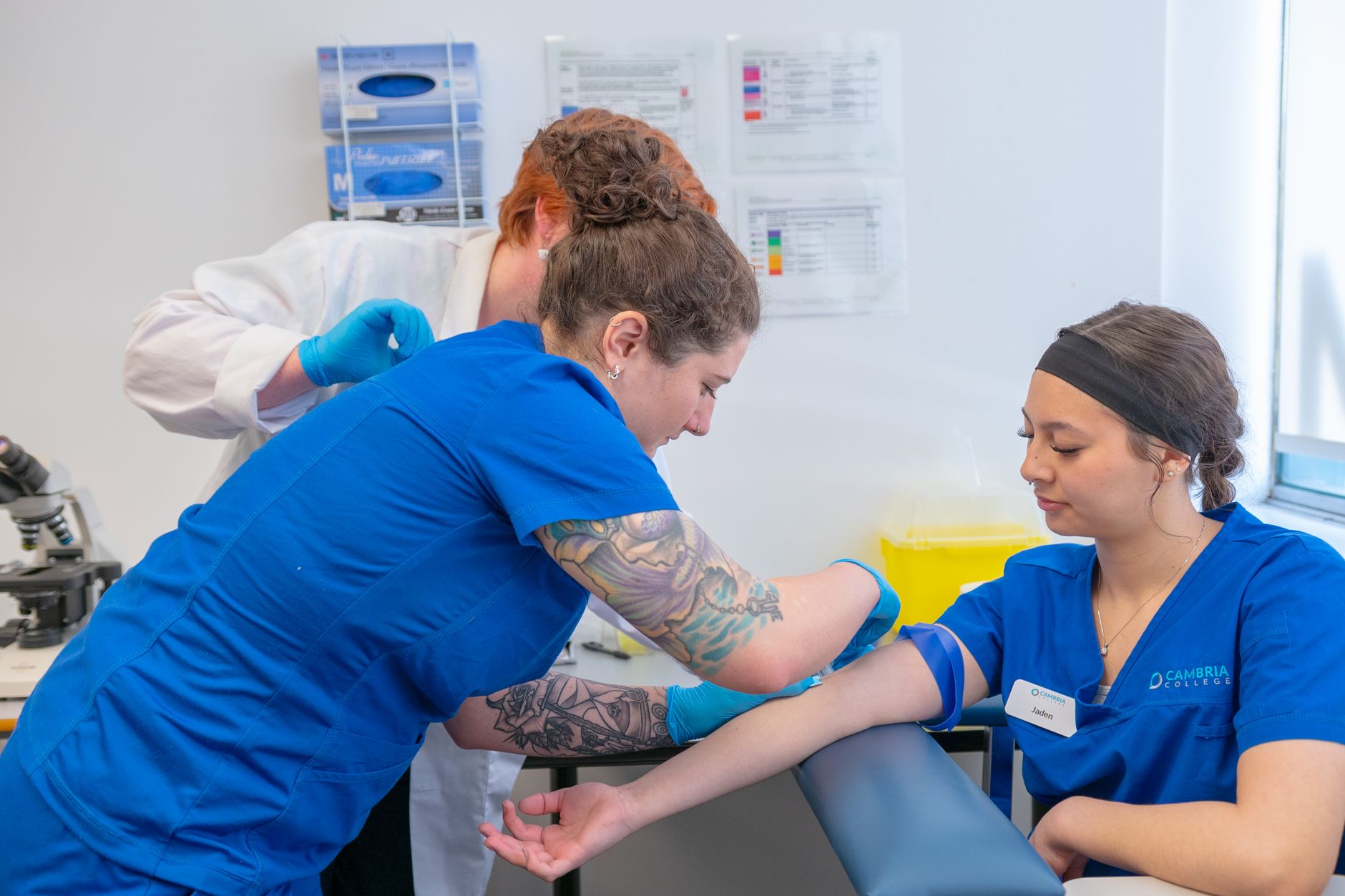 Nursing students practice blood draw techniques under supervision in a clinical lab.