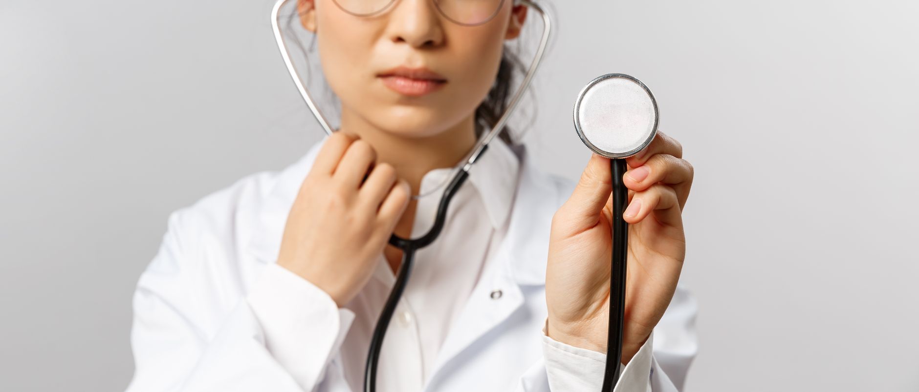 Close-up of a female doctor in a white lab coat, holding a stethoscope.