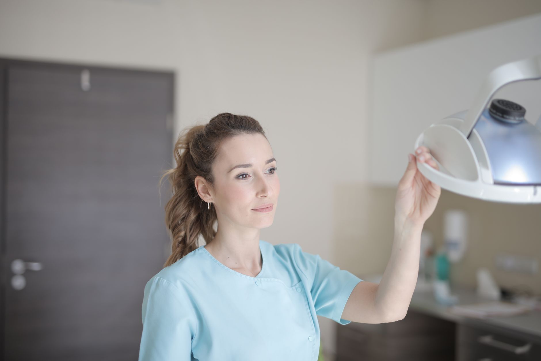 Positive young female doctor in uniform standing in modern clinic and holding lamp with hand while looking away