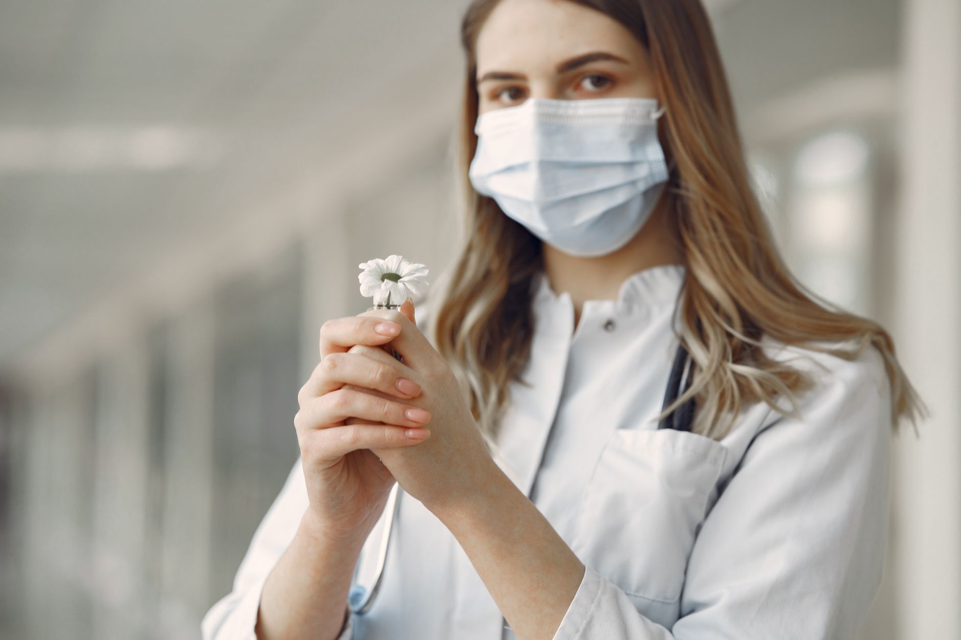 A young healthcare worker with a face mask holding a white flower, symbolizing hope and care.