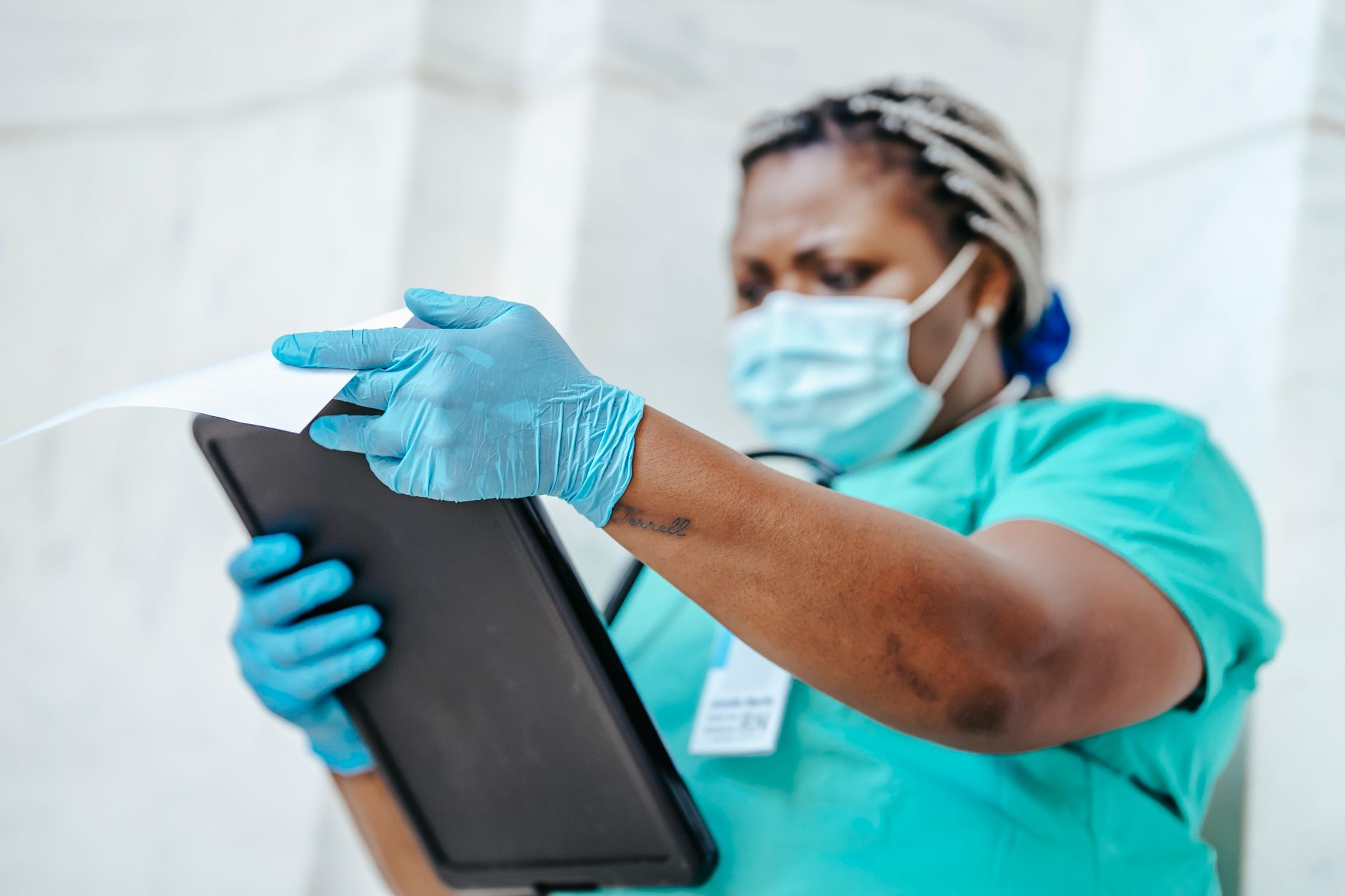 Middle aged African American female doctor in disposable gloves and mask reading paper on clipboard