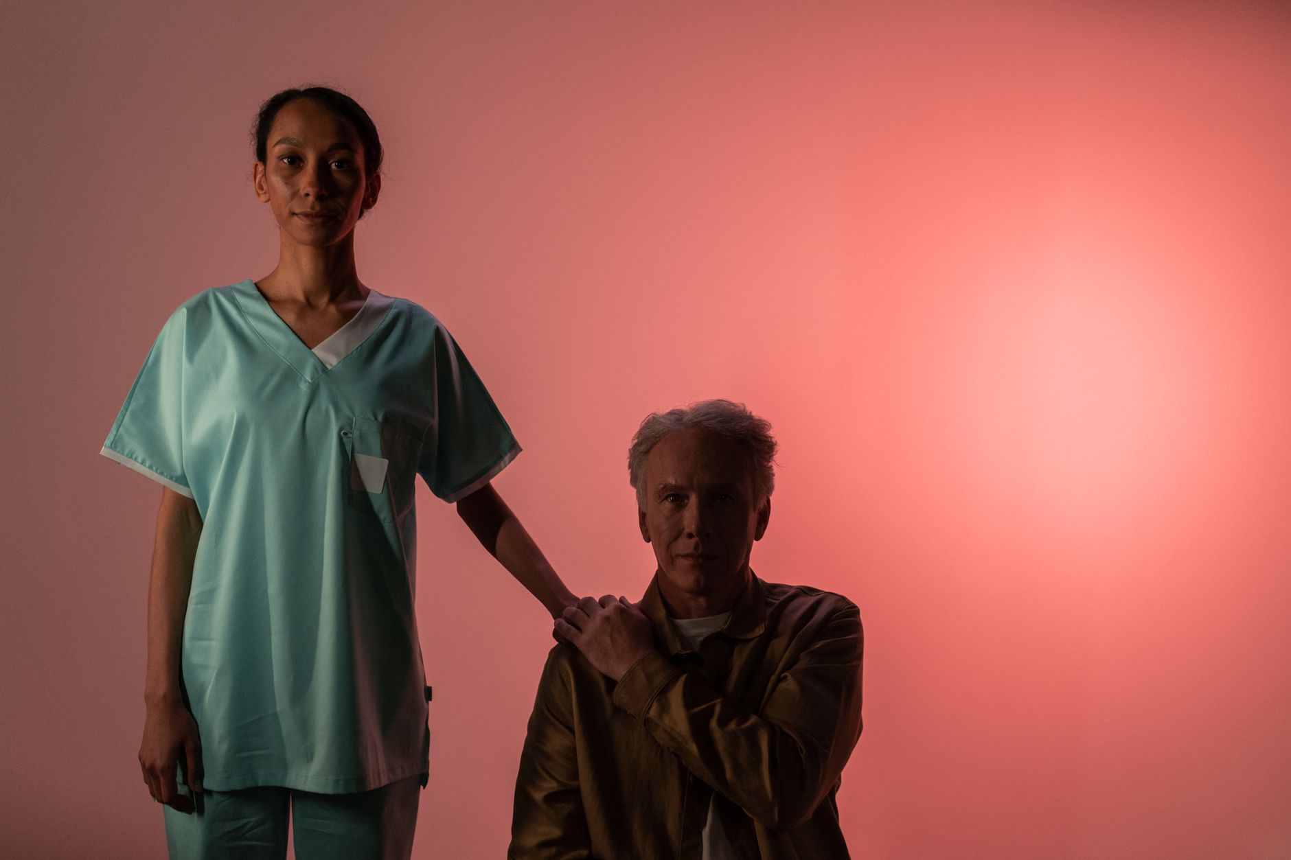 Nurse comforts elderly patient, symbolizing compassion and support. Studio setting with pink background.