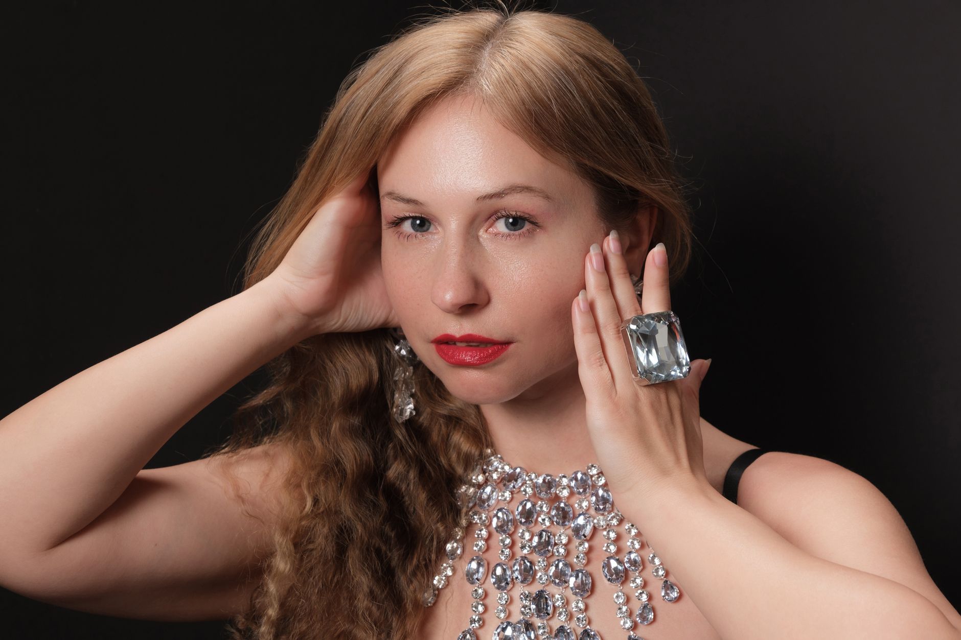 A sophisticated woman elegantly posing with a statement necklace and ring, exuding glamour.
