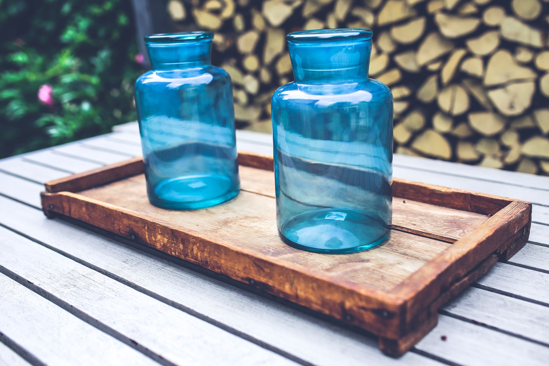 Two elegant blue glass jars sit on a rustic wooden tray on a garden table, perfect for home decor and relaxation.