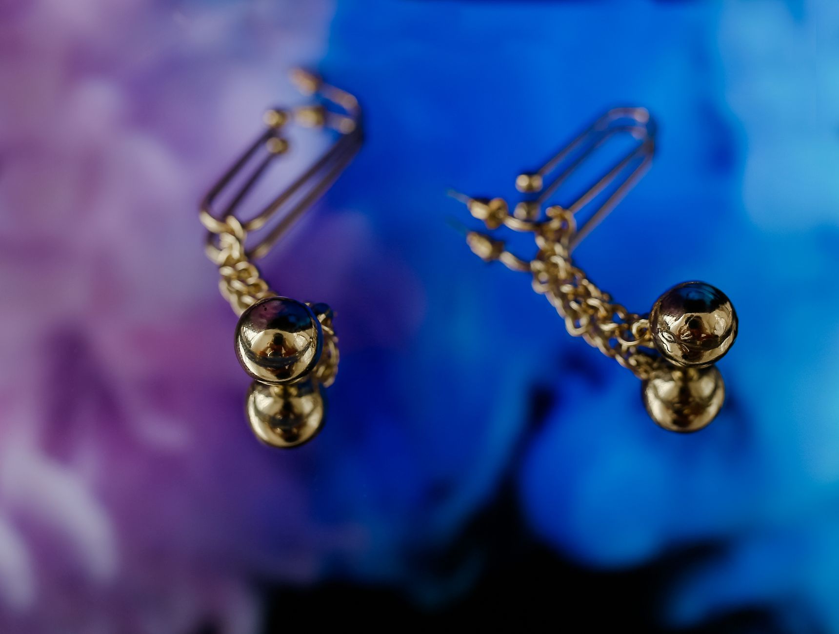 Elegant gold earrings with unique design against a vibrant gradient backdrop, showcasing luxury and style.