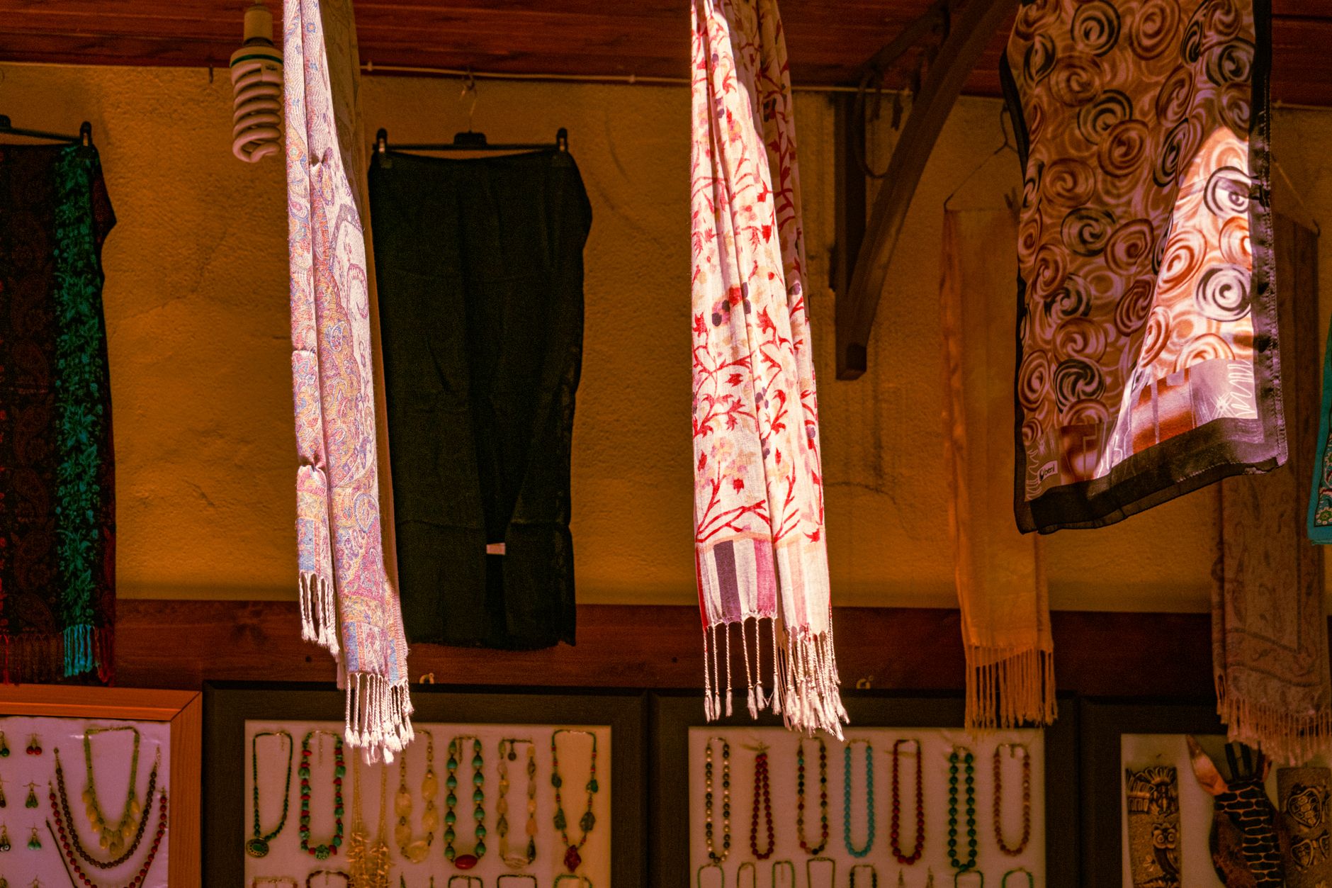 Vibrant fabrics and jewelry adorn a city market stall offering diverse cultural designs.