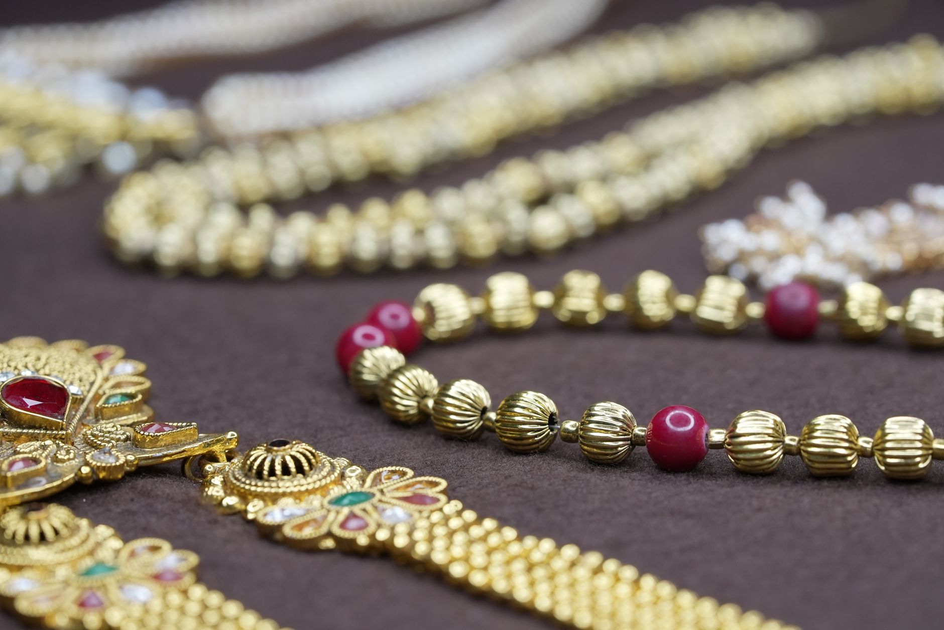 Close-up of exquisite gold and ruby jewelry arranged on a rich brown fabric, highlighting intricate details.