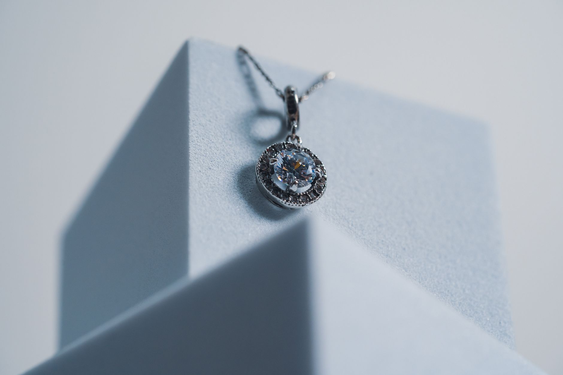 Close-up of a sparkling diamond necklace with intricate design on a minimalist geometric stand.
