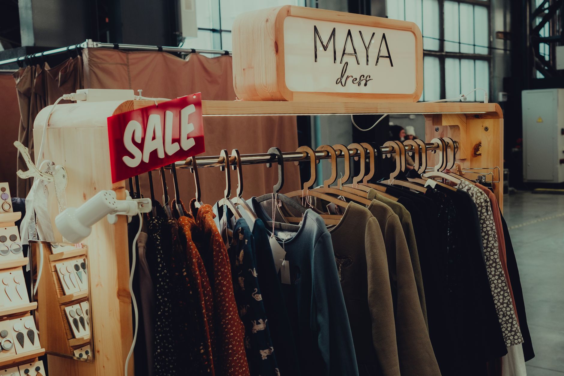 Assorted modern clothing hanging on hangers on rack with Sale inscription in spacious shop with dressing rooms and various accessories