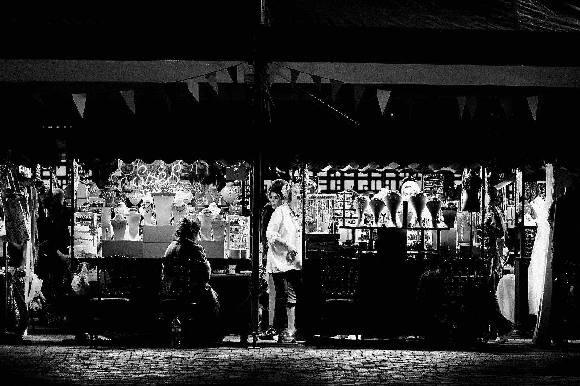 Black and white photo of a vibrant night market jewelry stall showcasing necklaces and accessories.