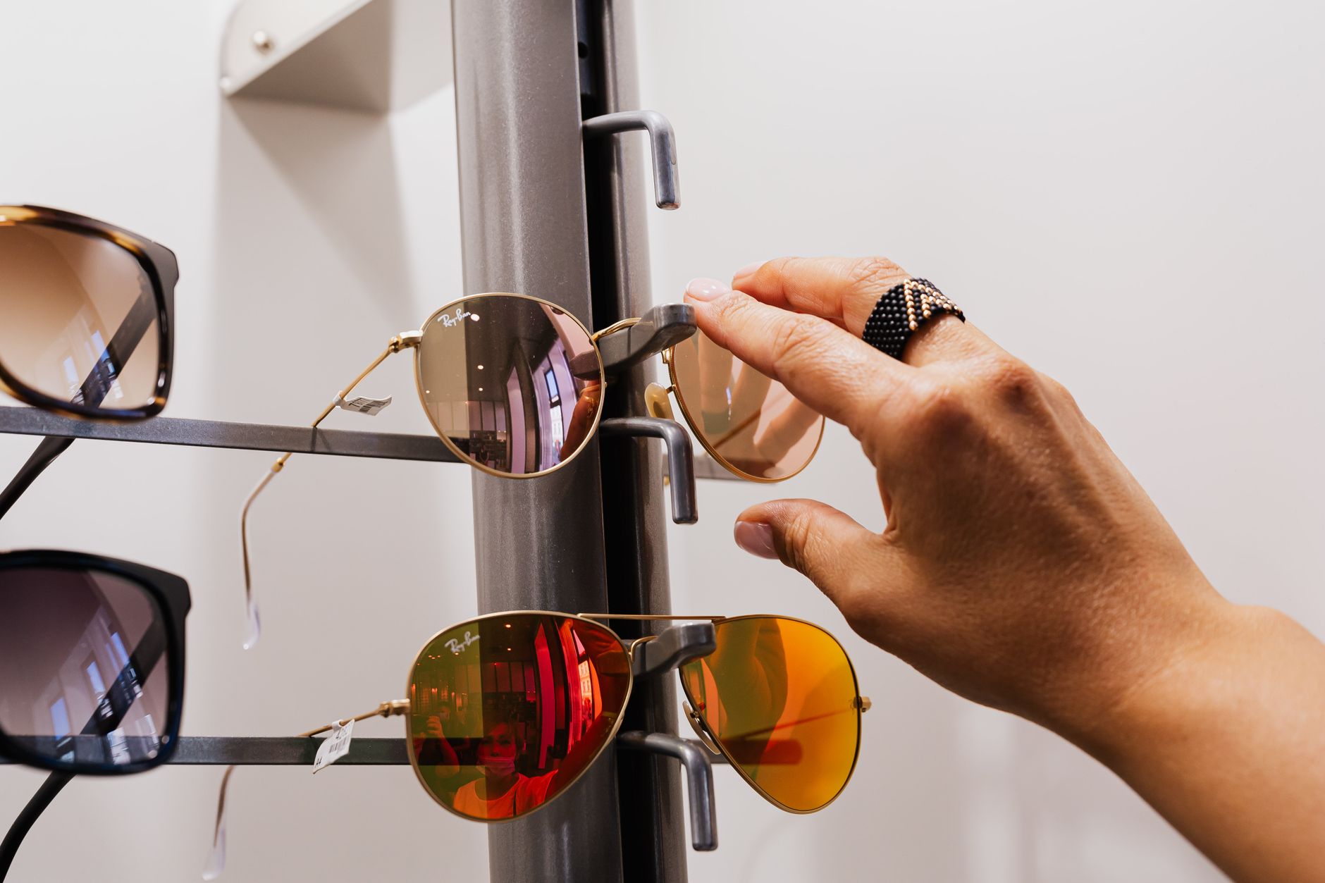 Close-up of a hand selecting sunglasses from a retail display with multiple choices available.