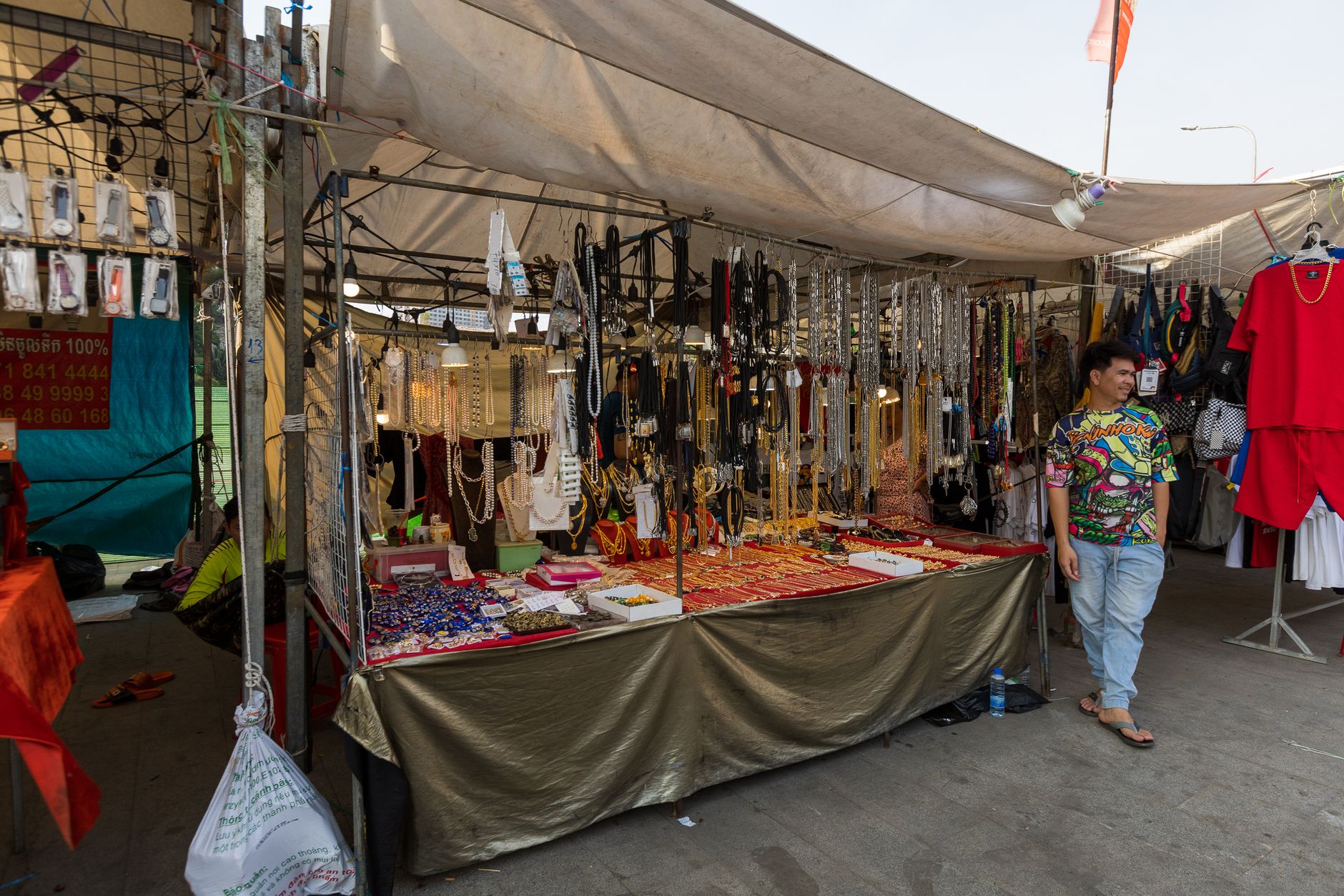 Colorful street market jewelry stall with a variety of accessories and a relaxed seller.