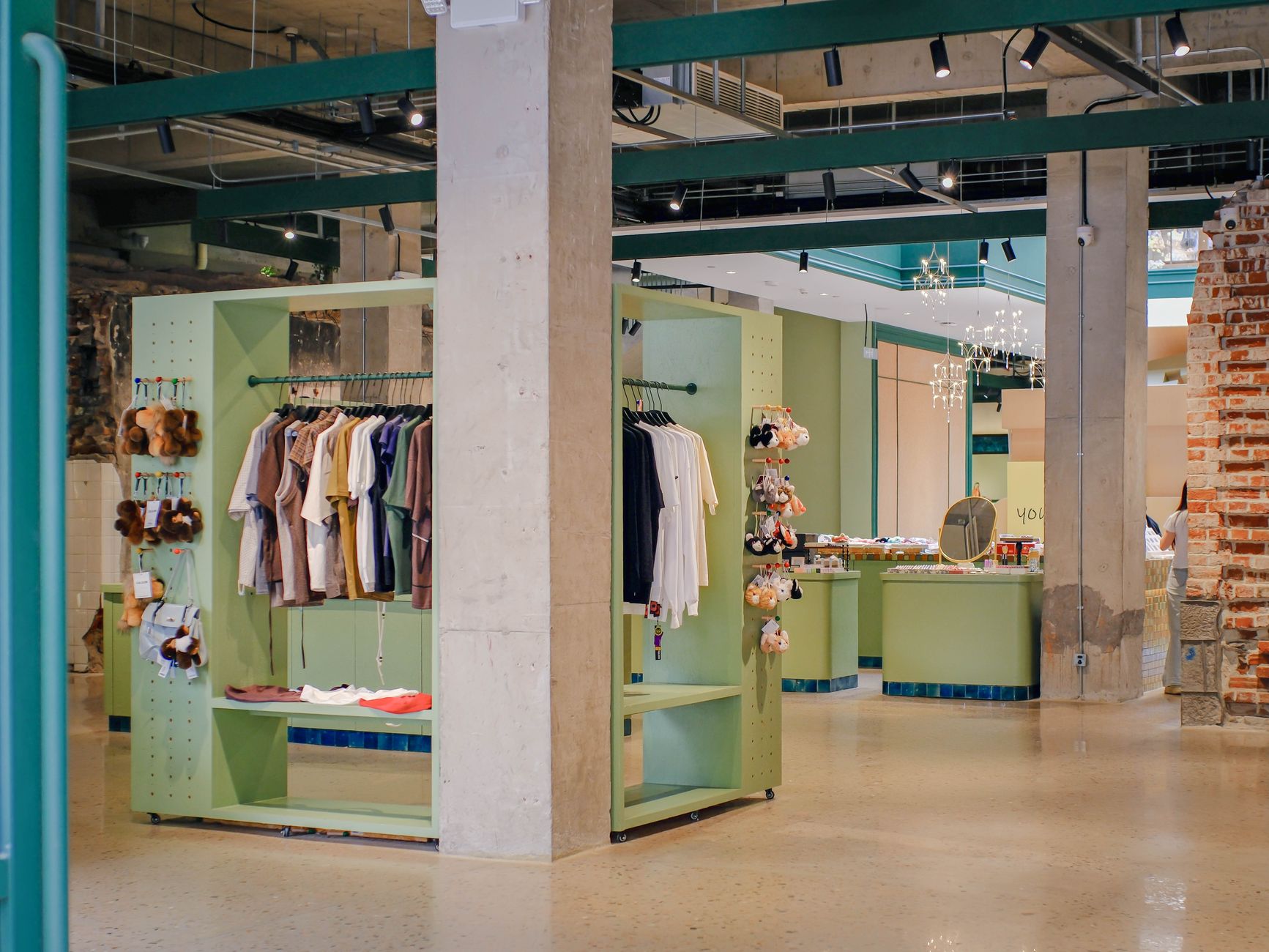 A contemporary store interior featuring minimalist green displays with hanging clothing and plush toys.