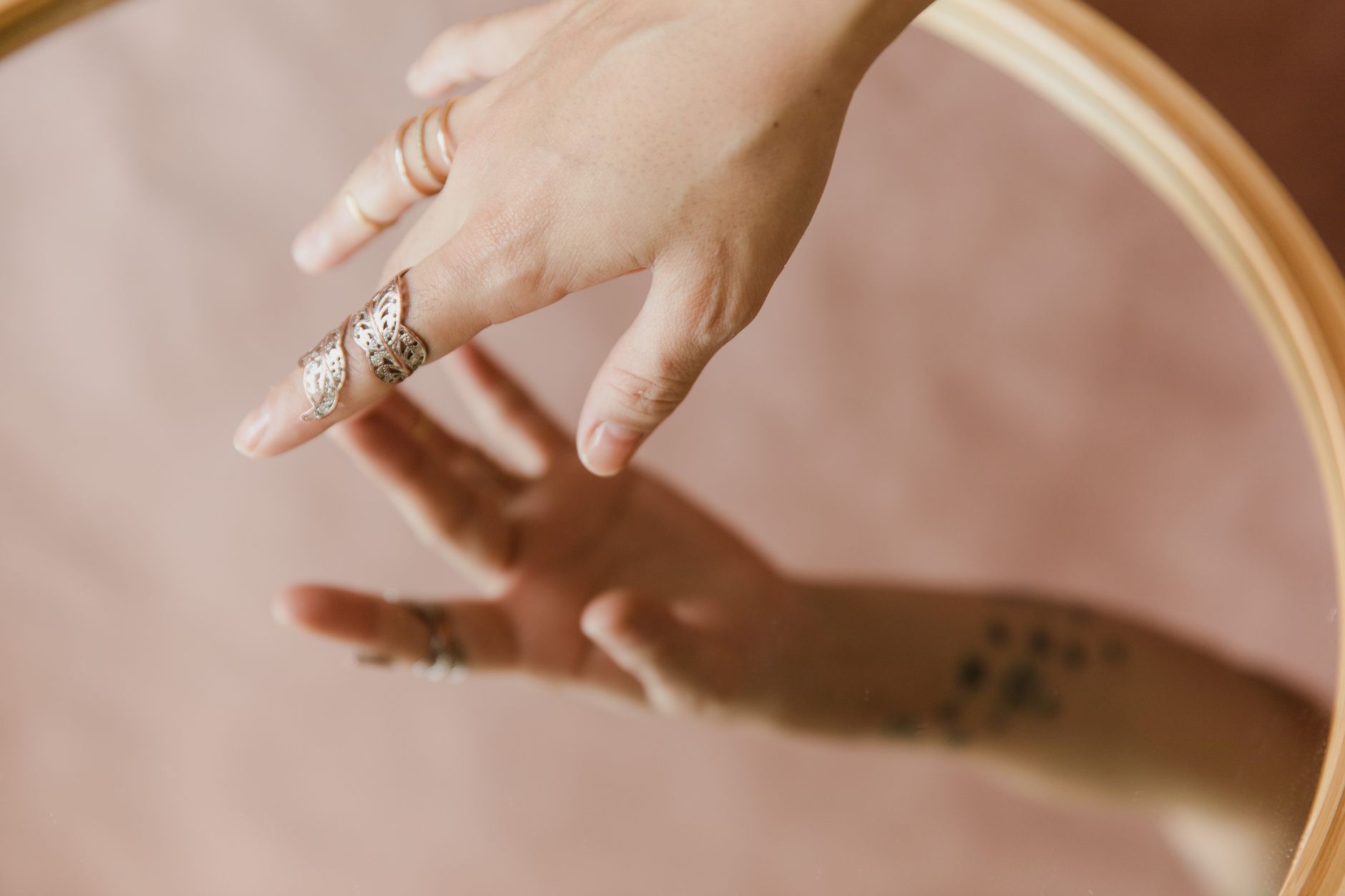Close-up of a hand wearing silver rings with a mirror reflection. Soft, elegant composition.