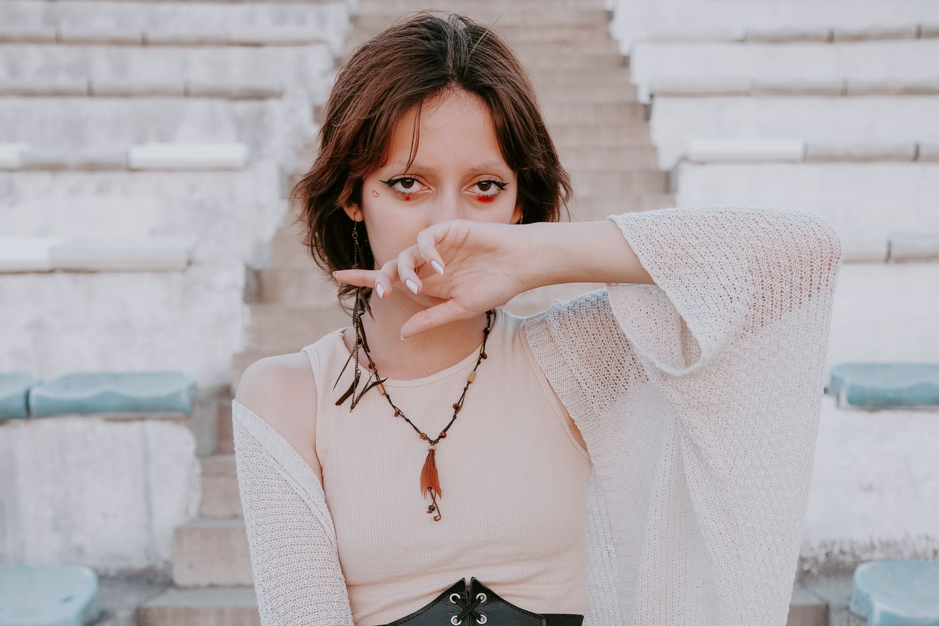 Fashion portrait of a woman with unique style, wearing a necklace and covering her face with hand.