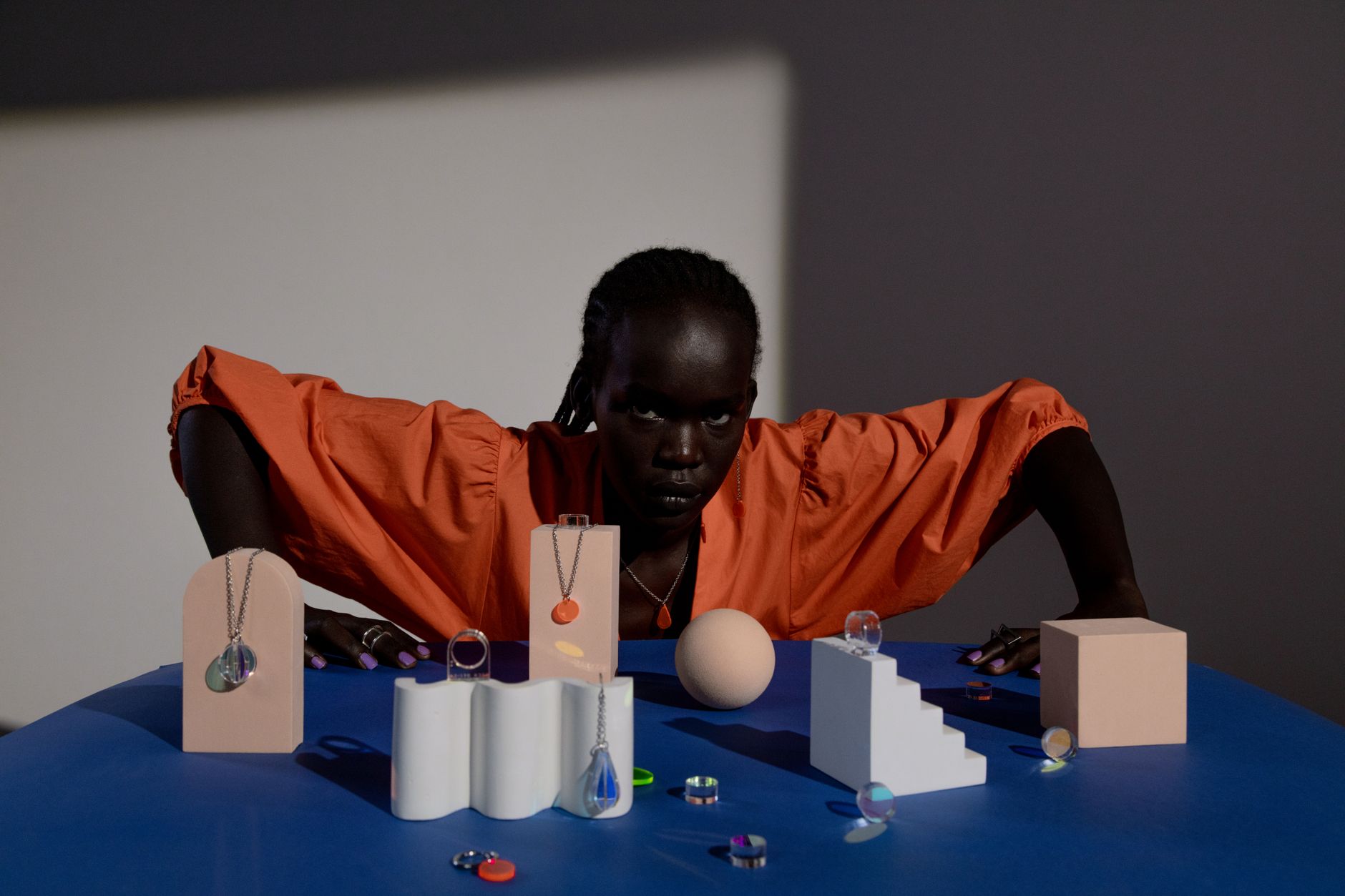 A striking portrait of a woman posing indoors with jewelry and geometric objects.