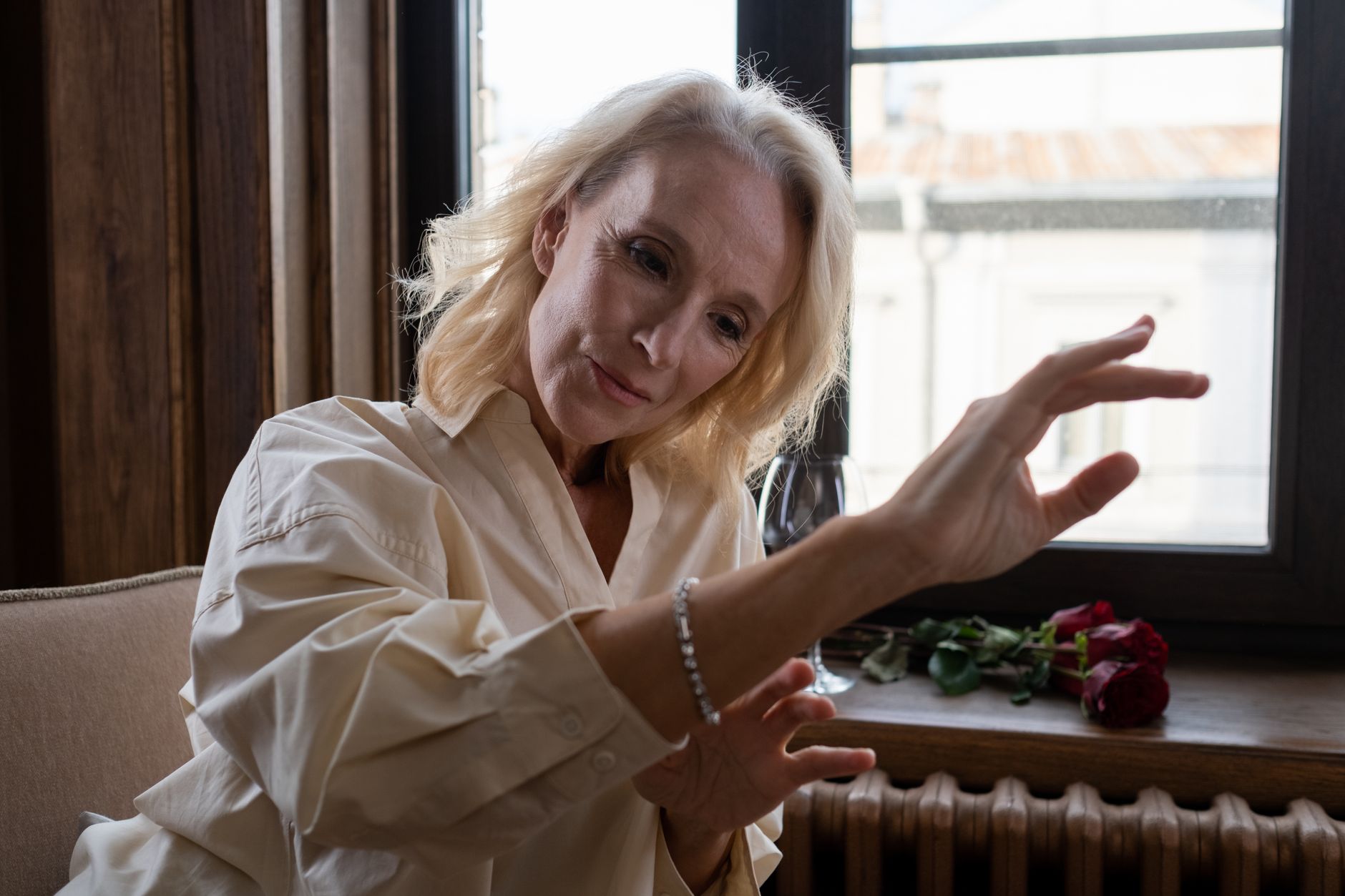 A serene woman admires her bracelet near a window, exuding elegance and contemplation.
