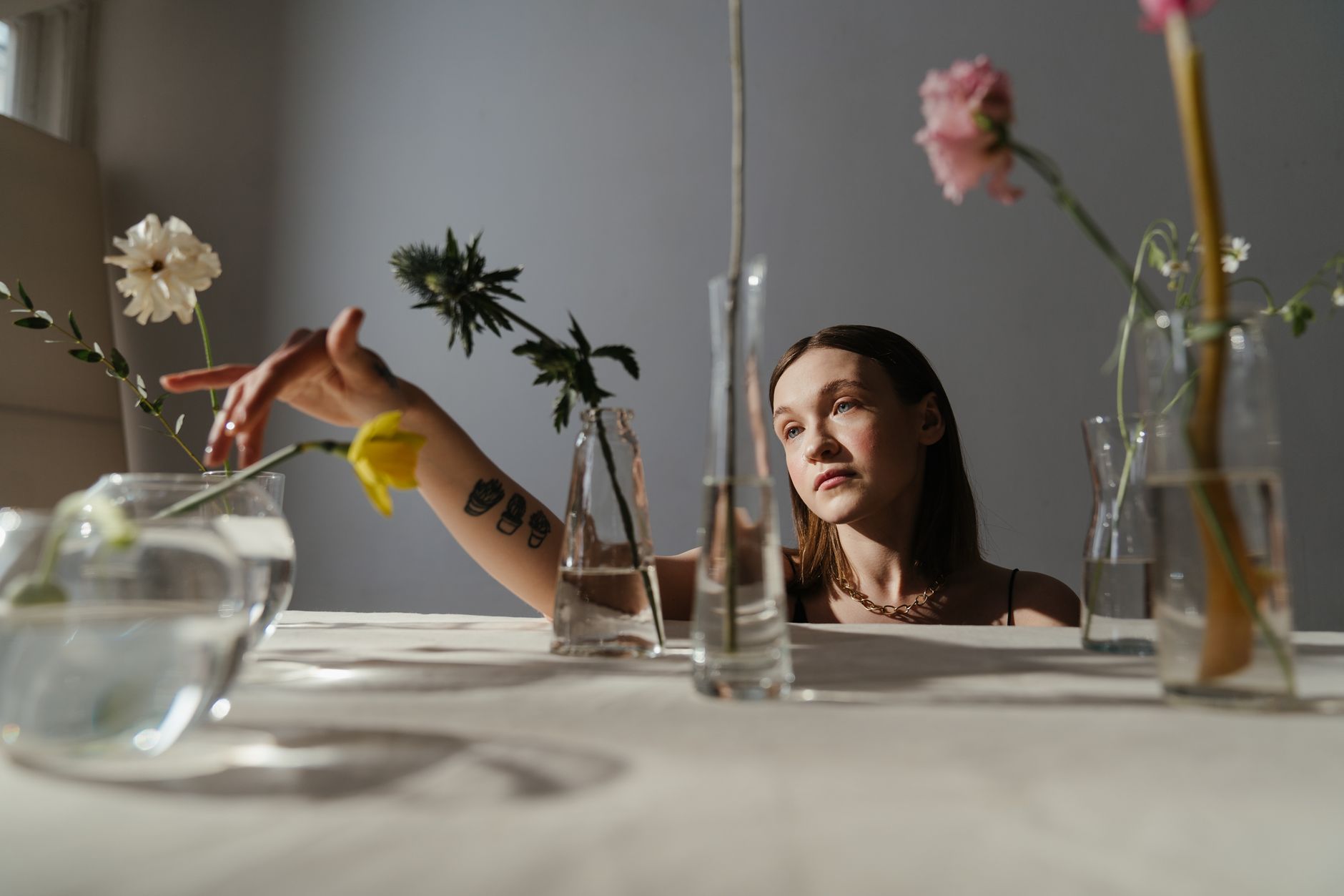 Thoughtful woman amidst artistic floral arrangements and glass vases, showcasing serene elegance.