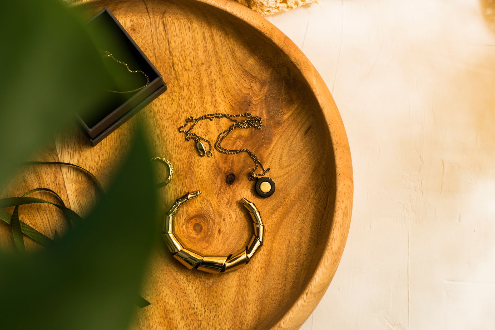 Minimalist jewelry set featuring necklaces and bracelets on wooden tray with greenery.