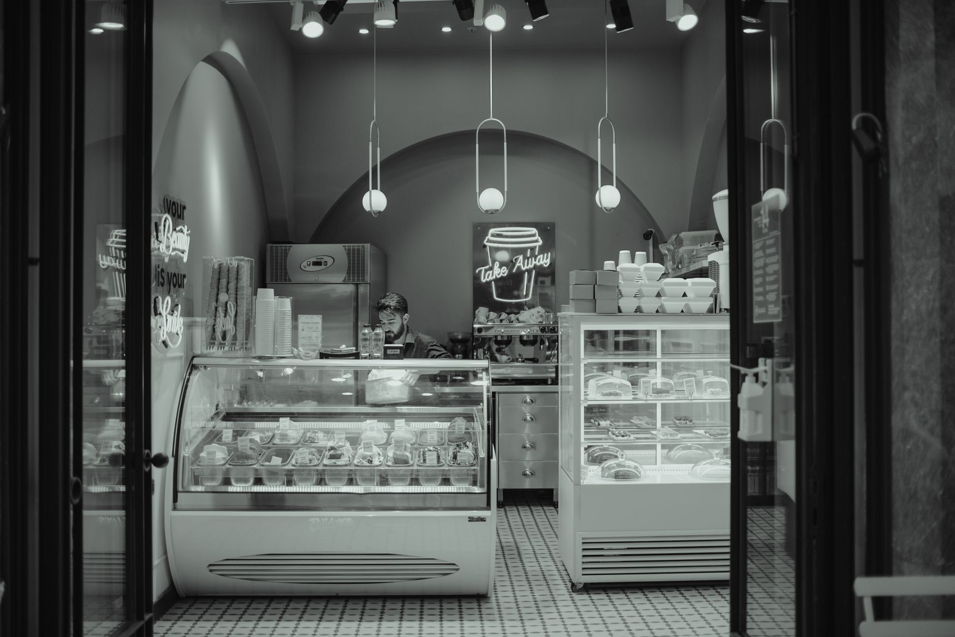 Monochrome view of a cozy bakery shop interior with takeaway sign, pastries, and modern lighting.