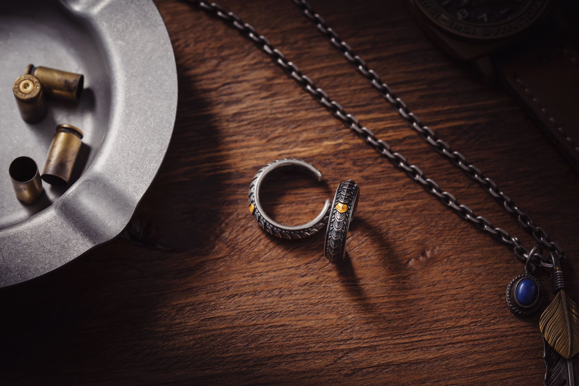 Artistic display of dragon scale cuff rings with an ashtray and chain on a wooden desk.