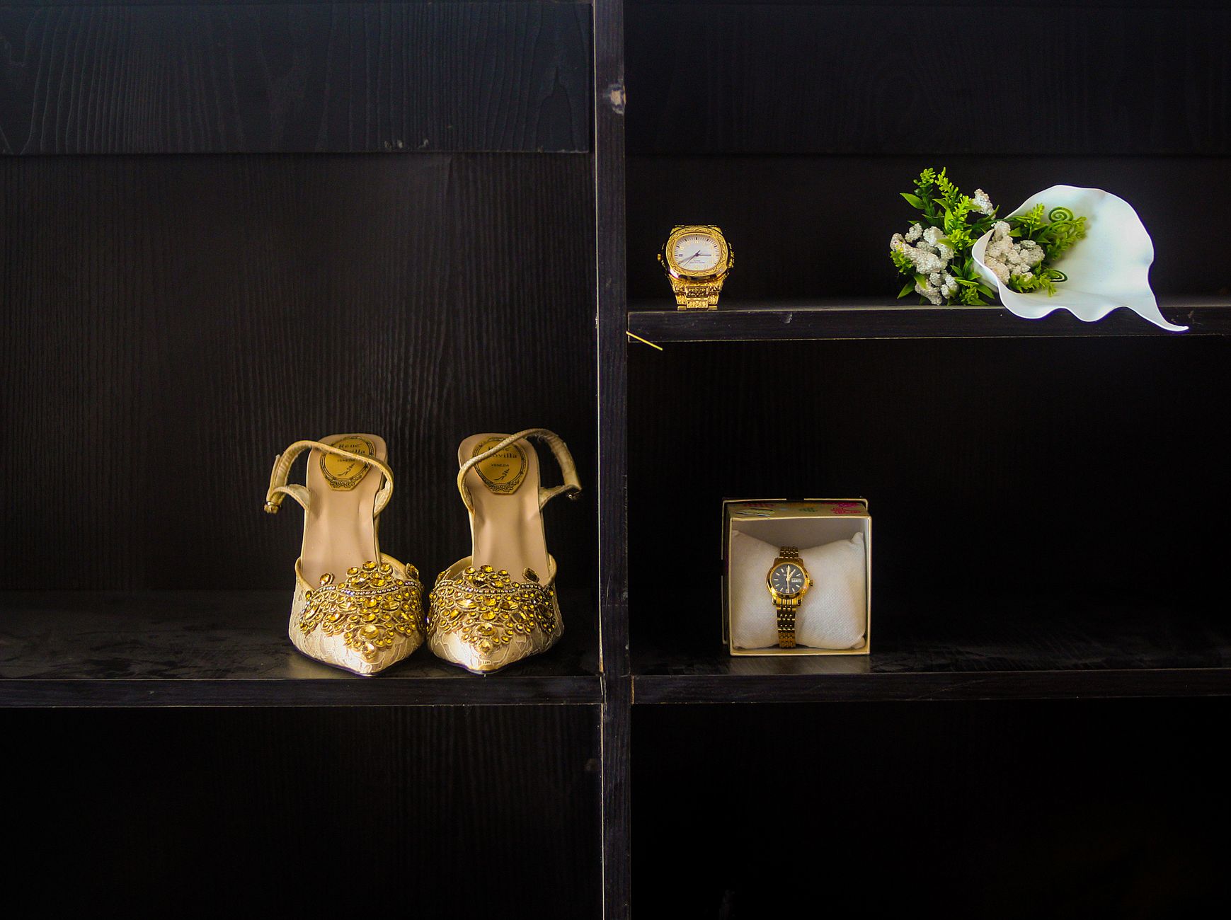 Sophisticated collection of golden shoes, watches, and floral moments on dark shelves for a chic look.