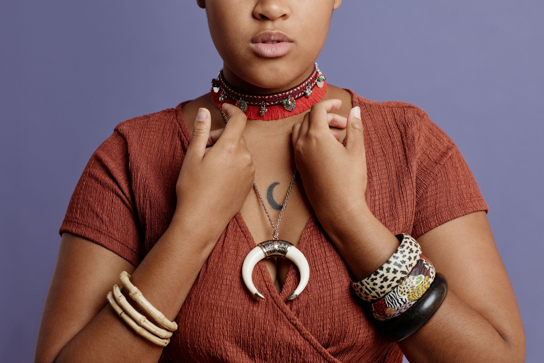 Fashionable woman showcasing unique jewelry, bracelets, and a moon choker necklace against a purple background.