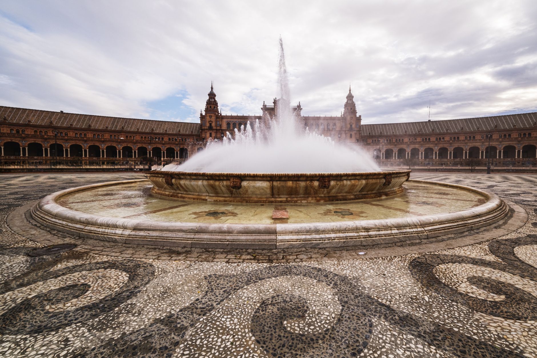 A stunning view of the Plaza de España fountain in Seville, showcasing its architectural grandeur on a cloudy day.