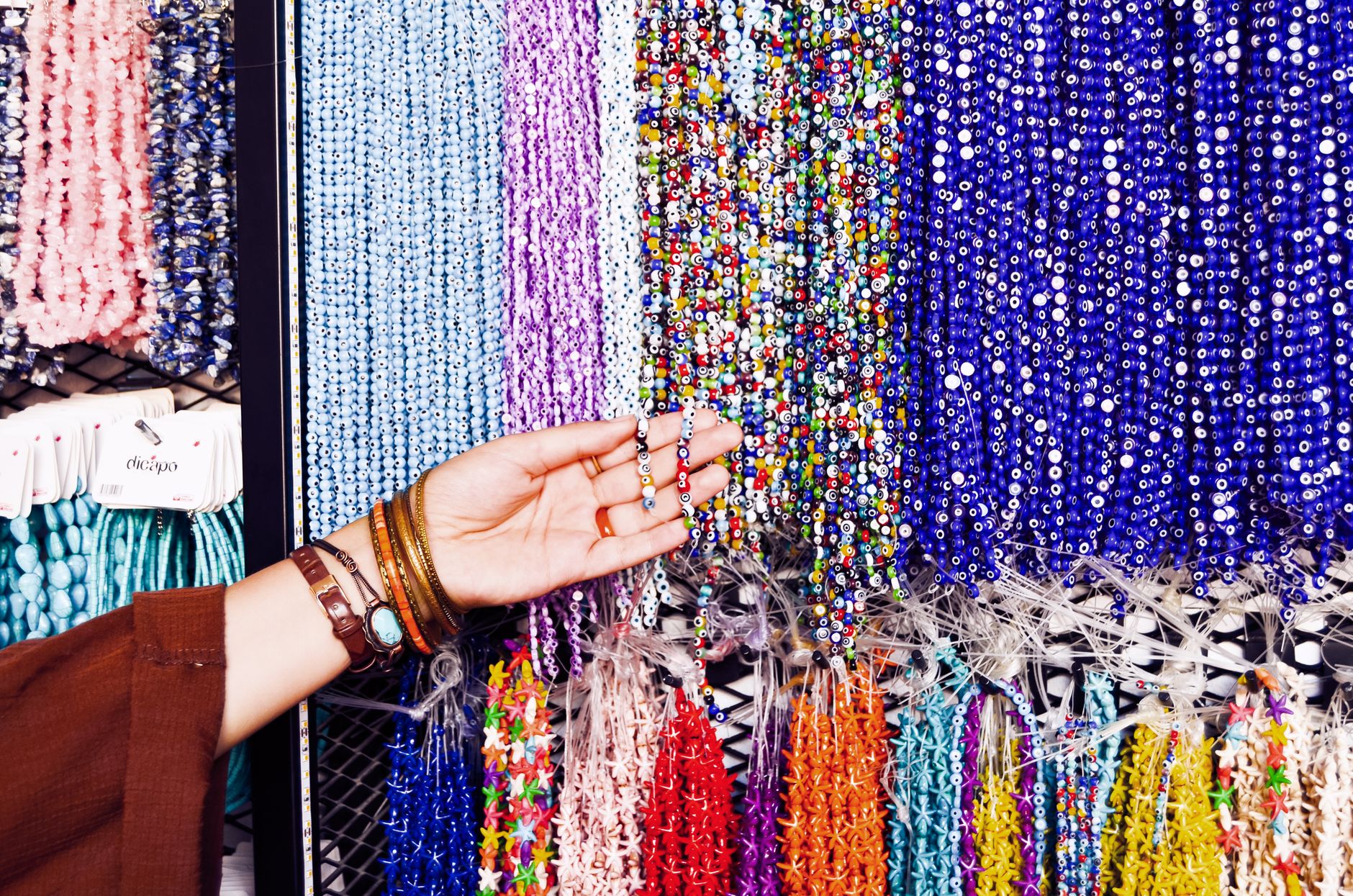 A vibrant collection of beads on display with a hand selecting a strand in a shop.