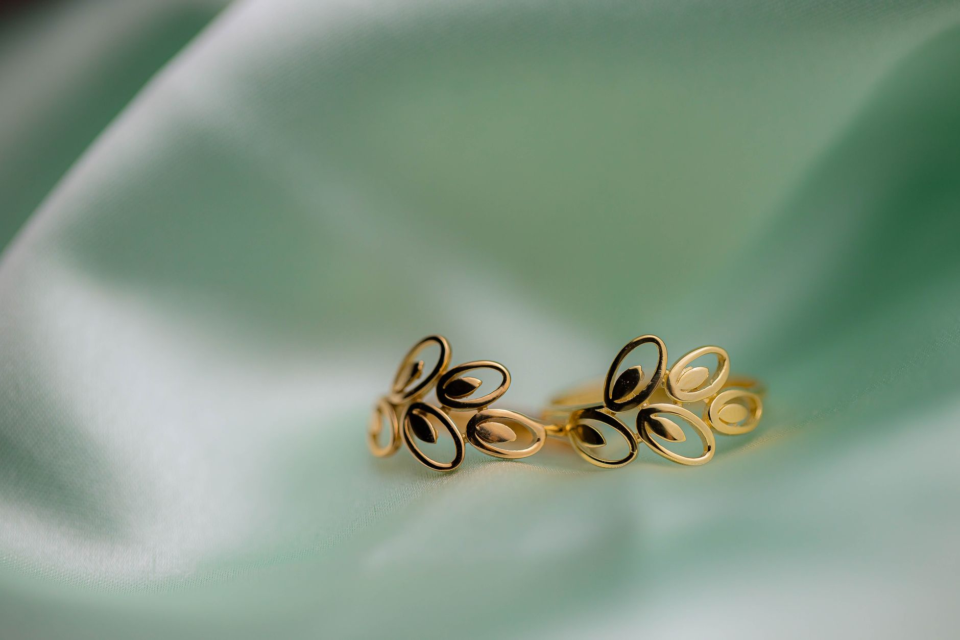 Beautiful handmade gold earrings displayed on a soft green fabric background, emphasizing their exquisite design.