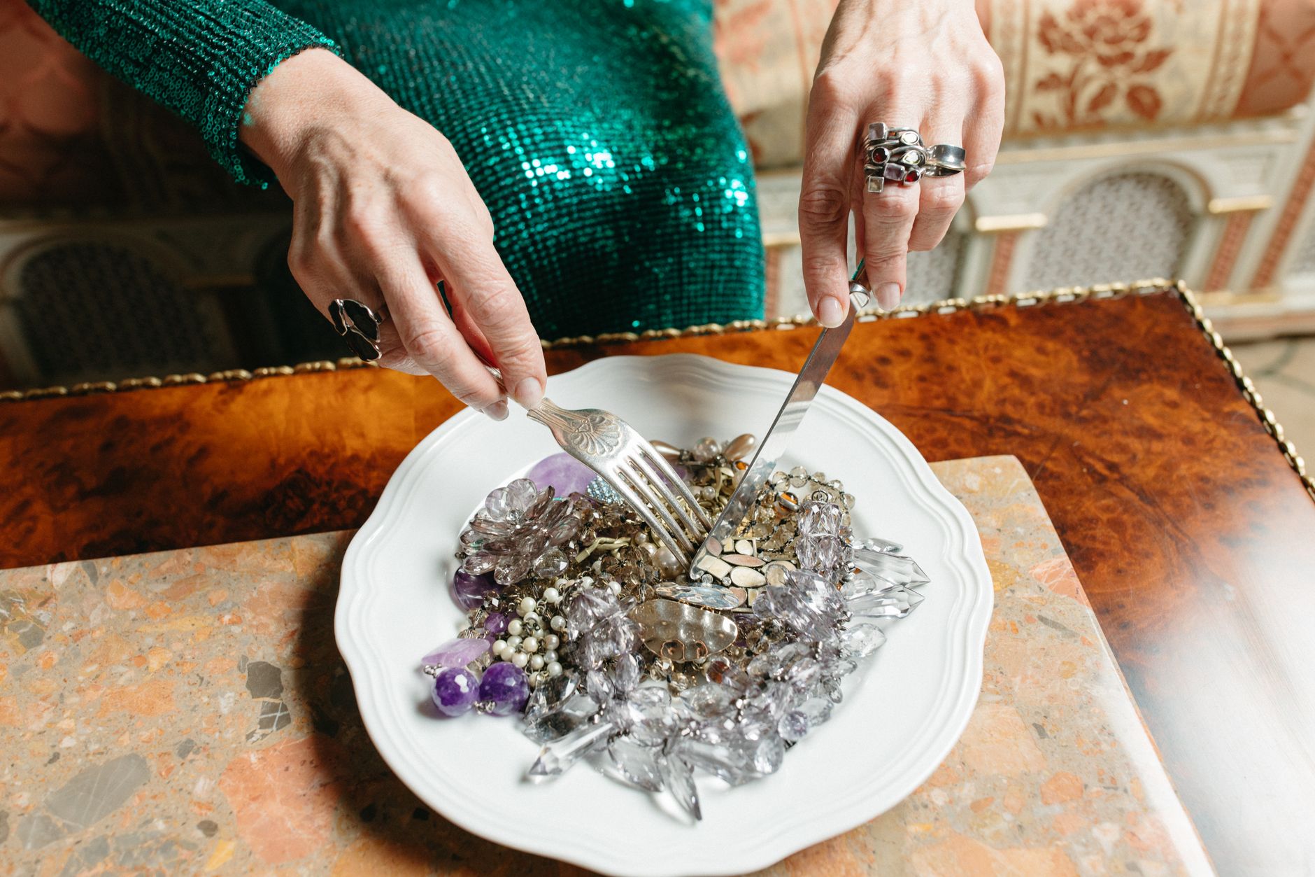 A unique dining setting featuring a plate of gems and jewelry on a marble table.
