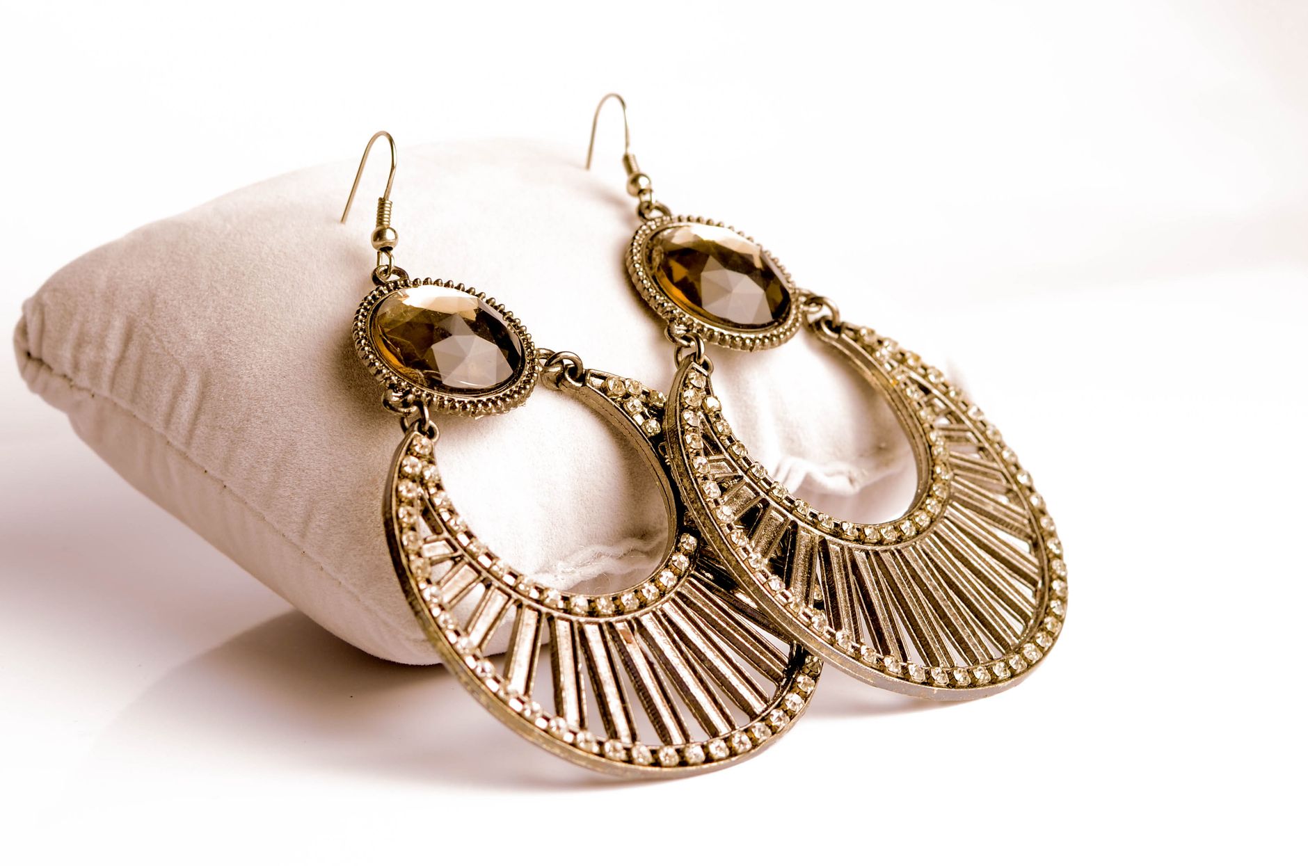 Close-up of intricately designed gold earrings resting on a plush white pillow for luxurious jewelry presentation.