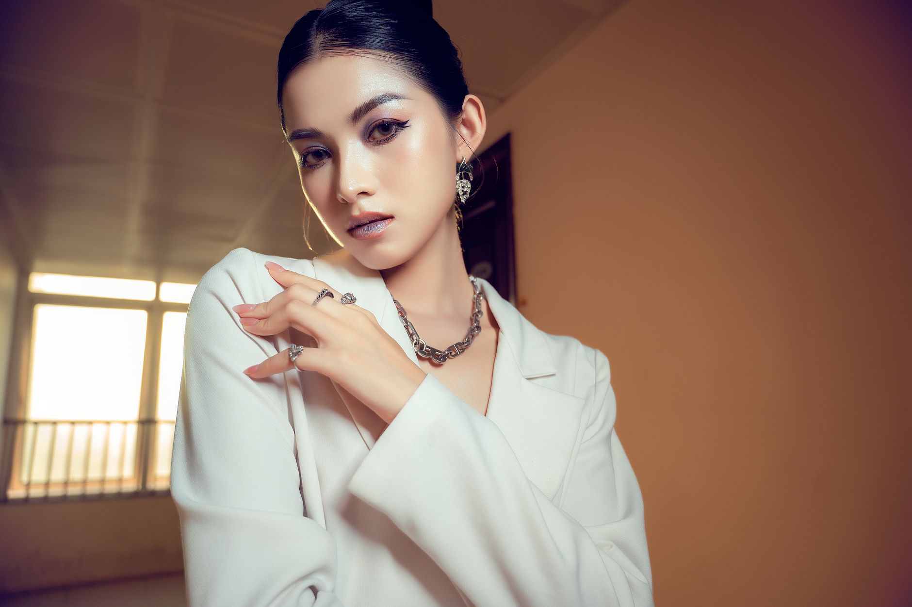A fashionable woman posing elegantly indoors, showcasing jewelry and style.