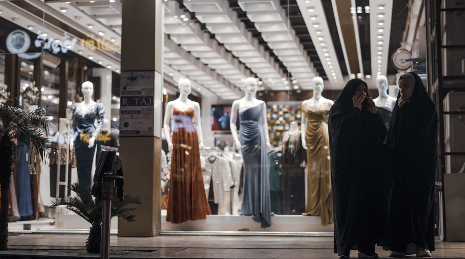 Fashion display with mannequins and shoppers outside a store at night.