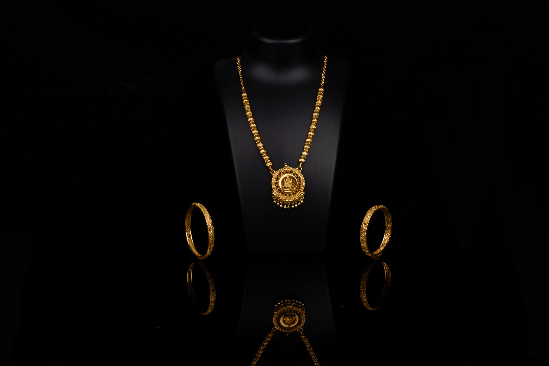 Luxurious gold necklace and bangles elegantly displayed against a dark backdrop, reflecting opulence.