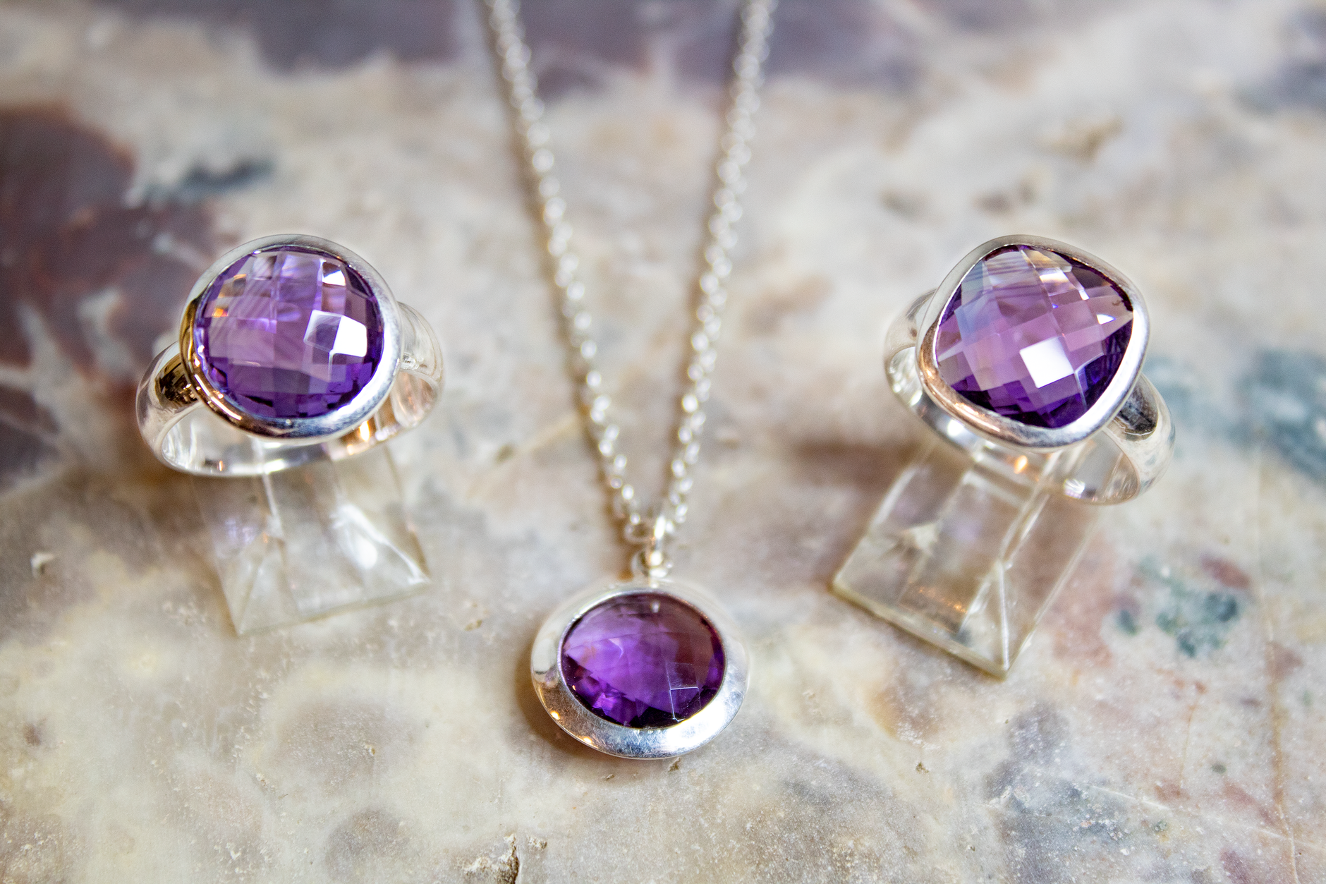 Close-up of amethyst rings and necklace set on a textured surface, showcasing silver accents.