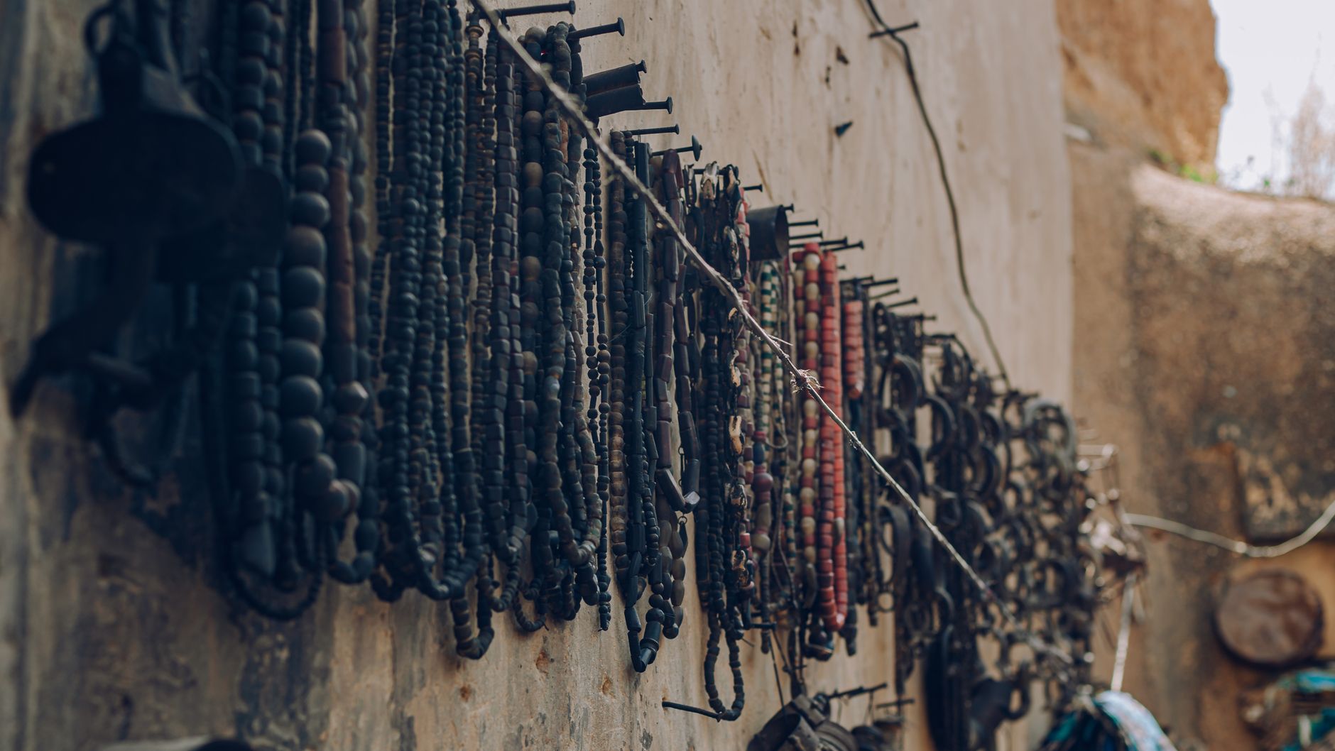 Vintage beaded jewelry hangs on an outdoor wall, showcasing intricate designs and craftsmanship.