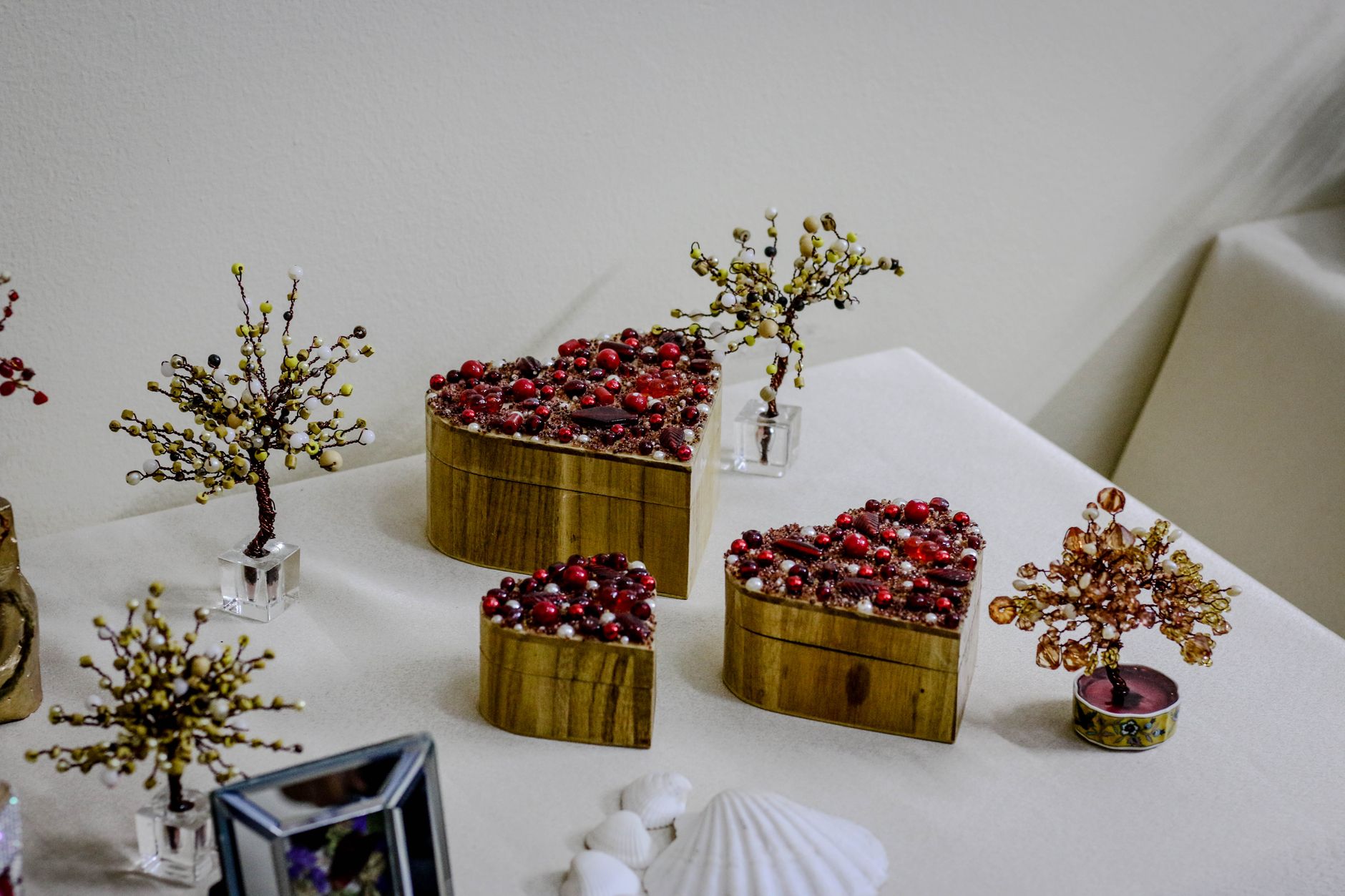 Heart-shaped wooden boxes adorned with red beads, surrounded by decorative trees on a white surface.
