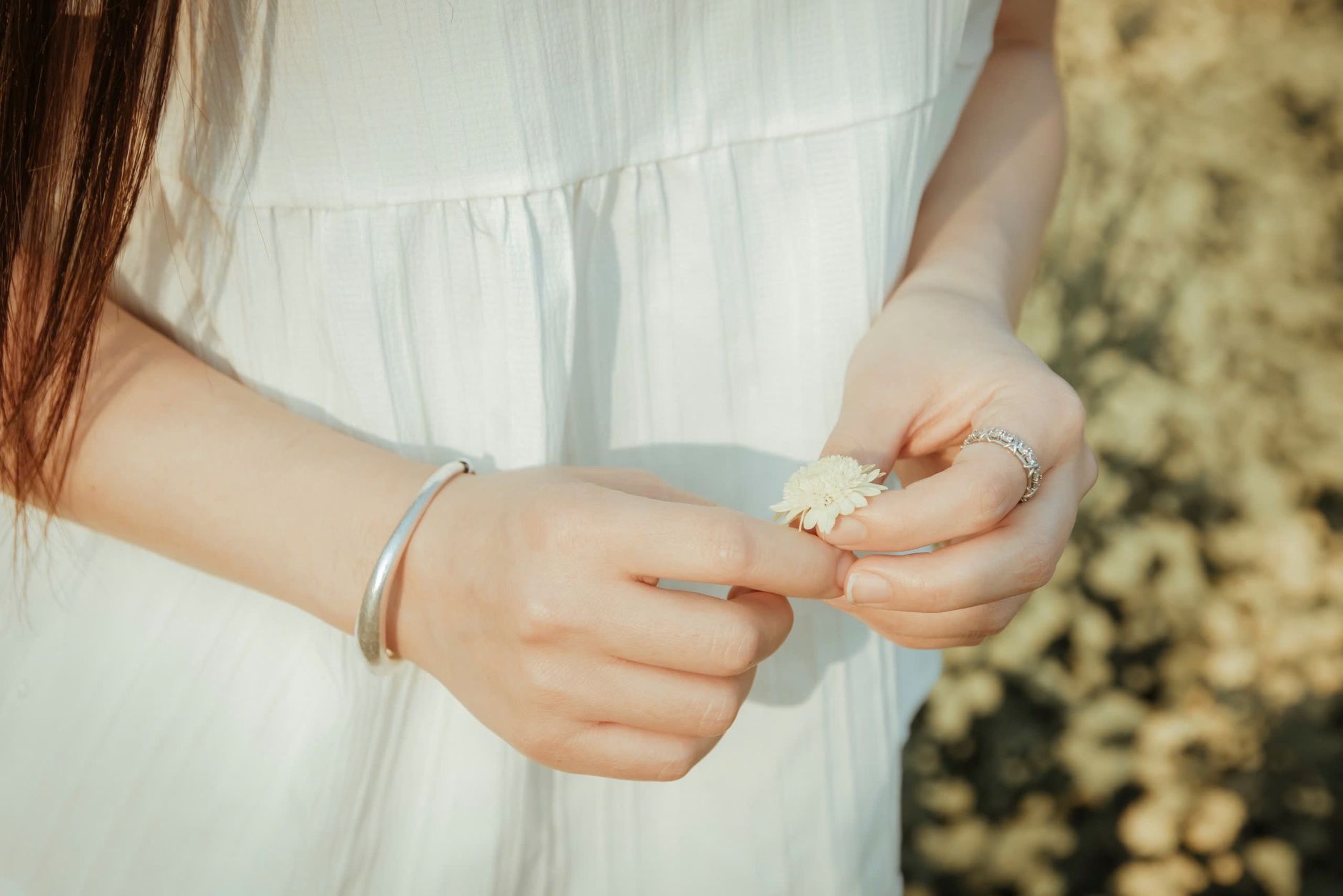Tranquil moment with a woman in white holding a small flower, embodying simplicity.