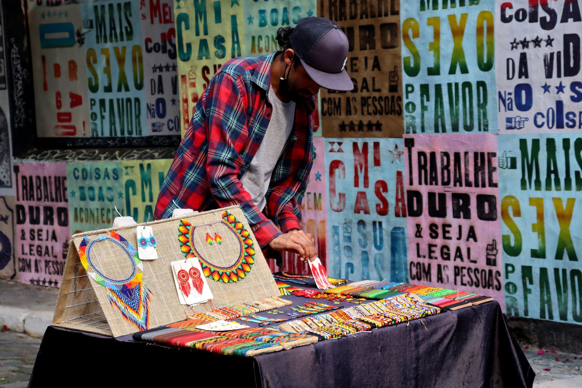 A street vendor arranges handcrafted jewelry against a vivid urban backdrop with bold typography.