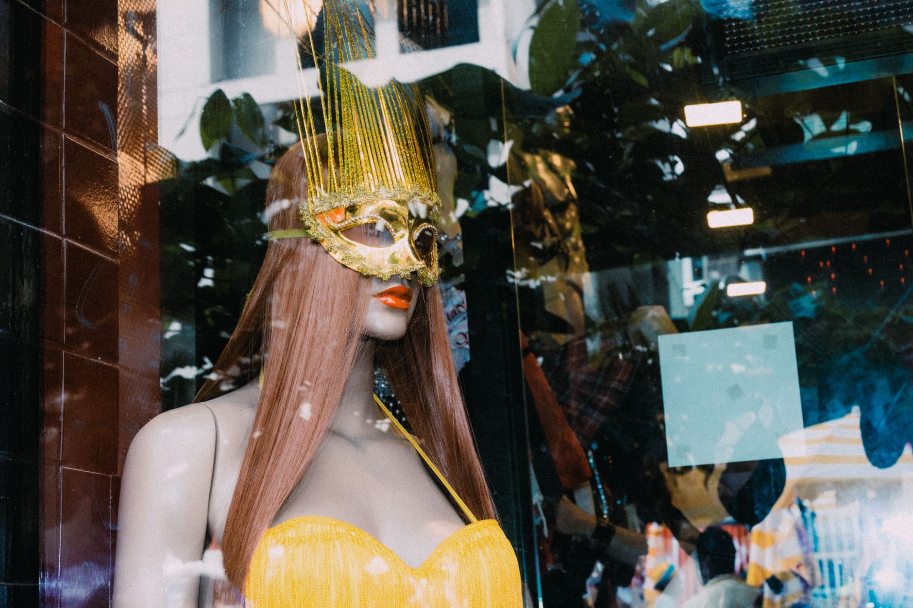 A mannequin adorned with a golden mask and yellow outfit in a vibrant store window.