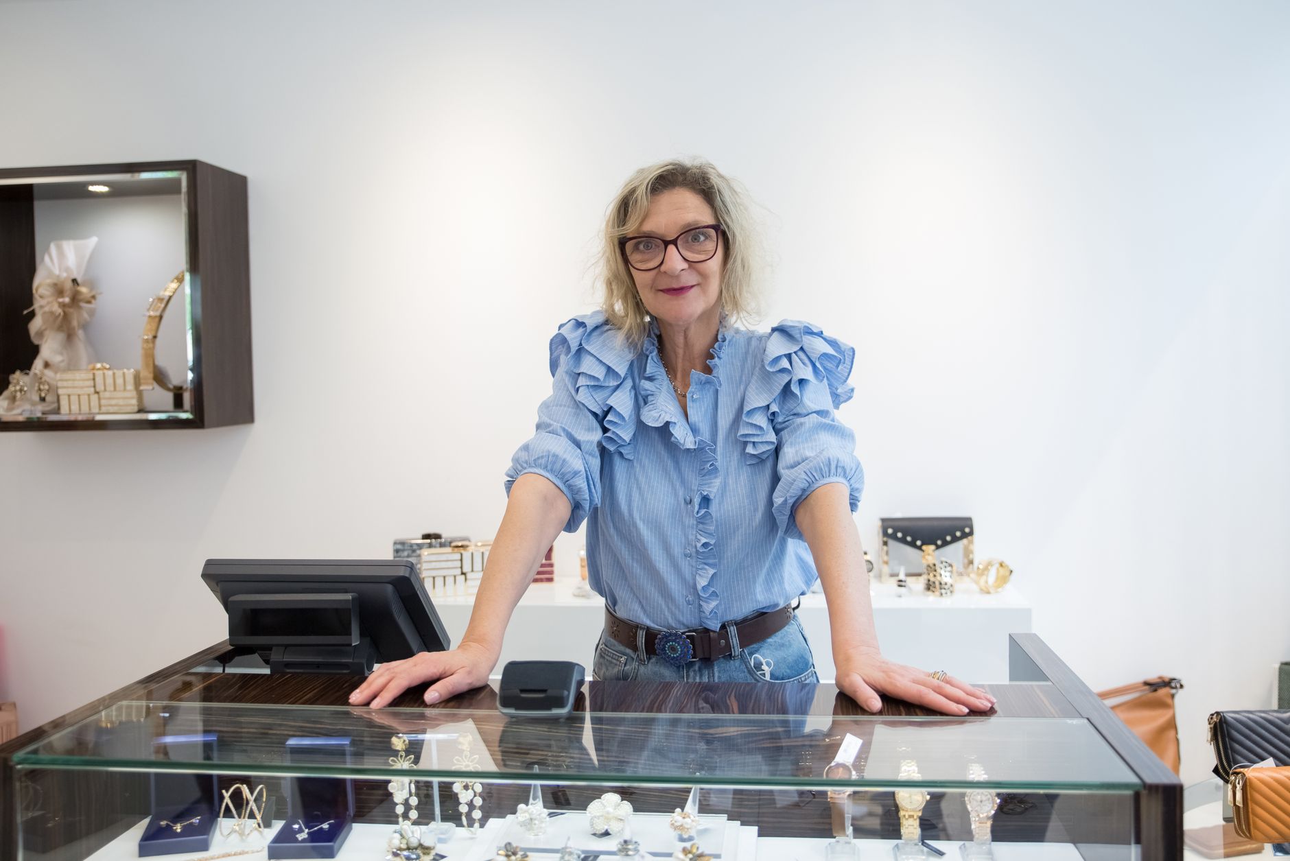 A senior woman stands confidently at a jewelry store counter in Portugal, showcasing elegance.