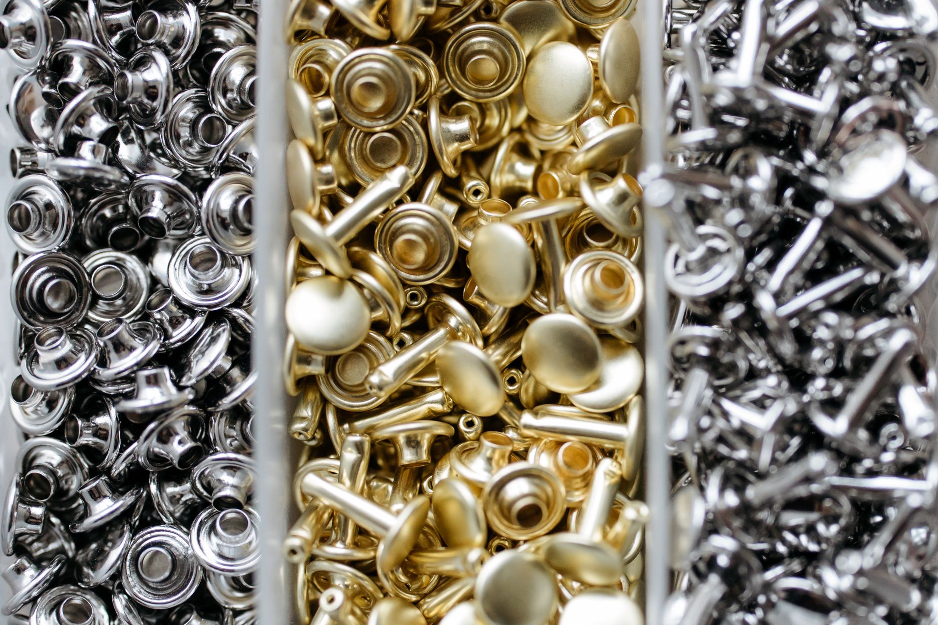Close-up view of gold and silver metal studs organized in bins for crafting or manufacturing.
