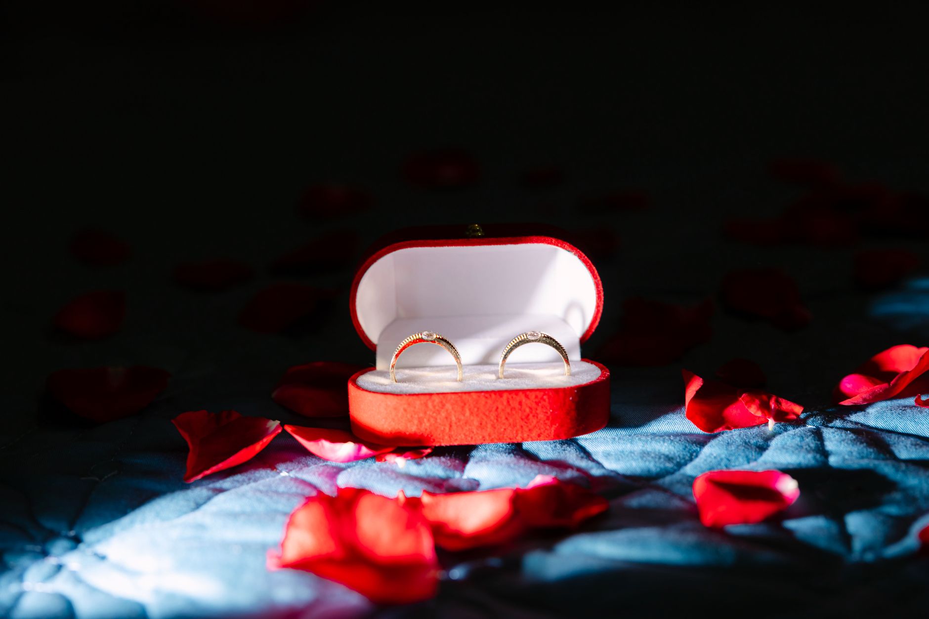 A pair of gold rings inside a red velvet box surrounded by rose petals, symbolizing romance.