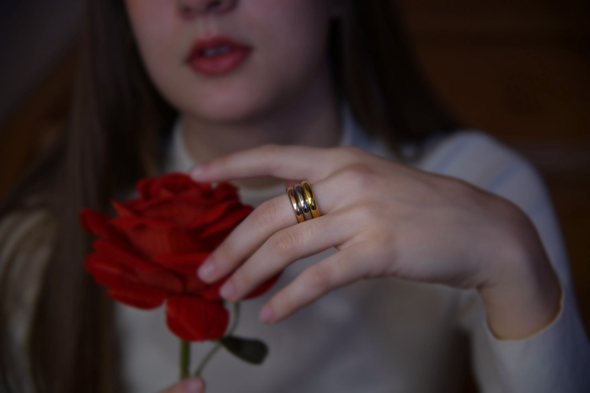 Close-up of a hand adorned with gold rings gently holding a red rose, showcasing elegance and style.