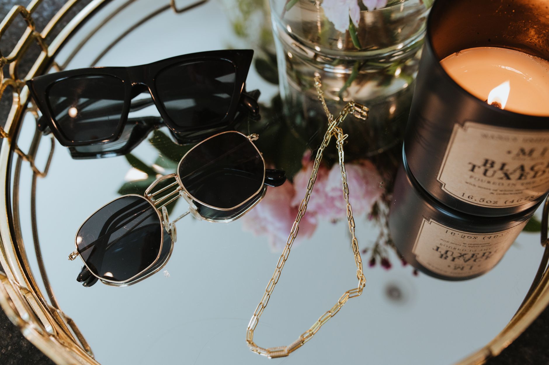 Elegant display of sunglasses and candle on a mirrored tray, showcasing luxury accessories.