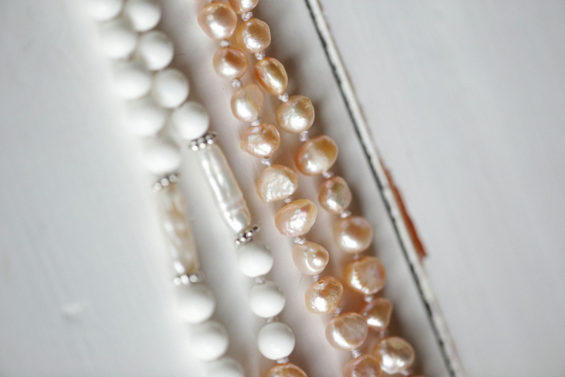 Close-up of elegant pearl and bead necklaces displayed on a white surface, showcasing delicate jewelry design.